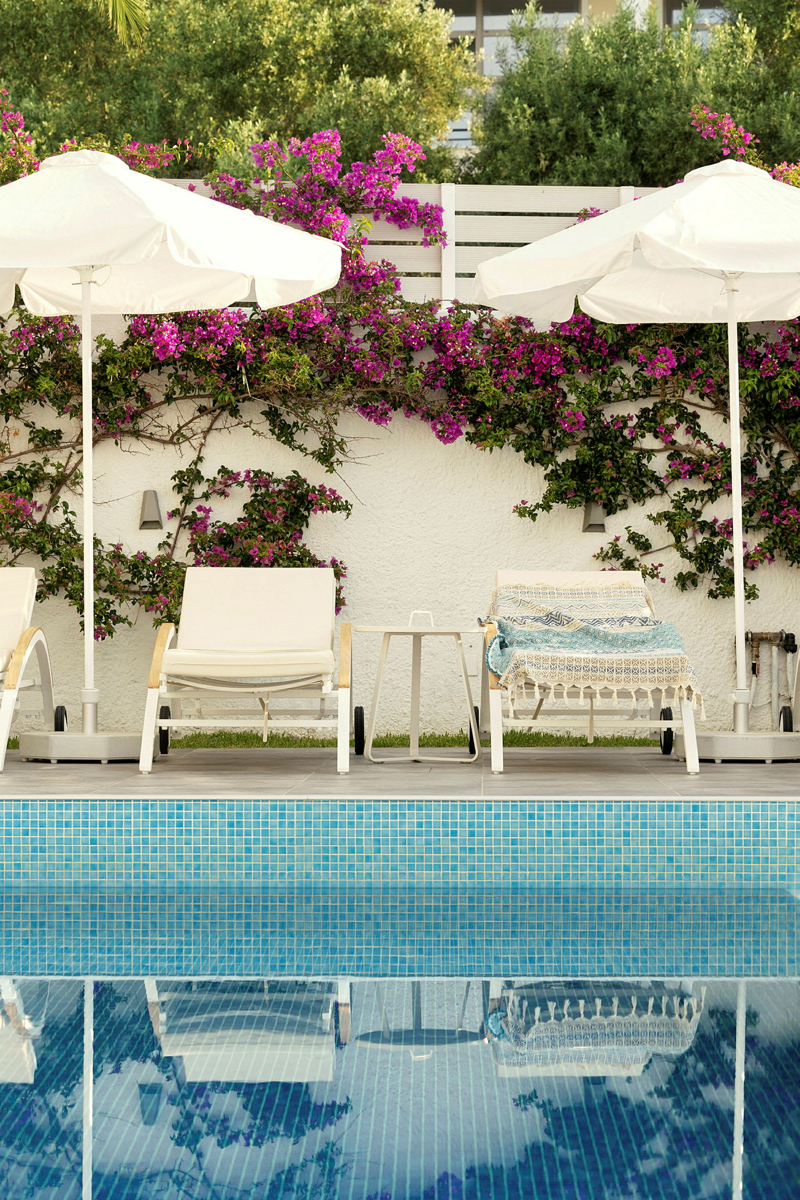Bild av solstolar och parasoller vid en pool, med en vägg dekorerad med blommor i bakgrunden. (AI-genererad text)