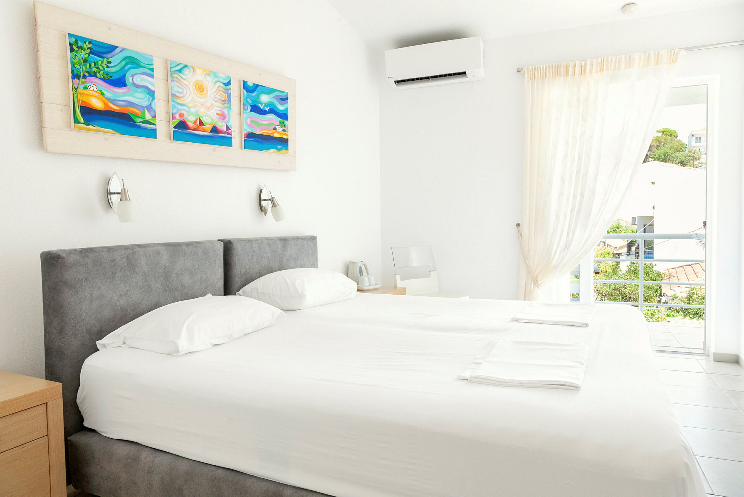 En ljus hotellrum med en dubbelsäng, konstverk på väggen och ett öppet fönster med utsikt. (AI-genererad text)