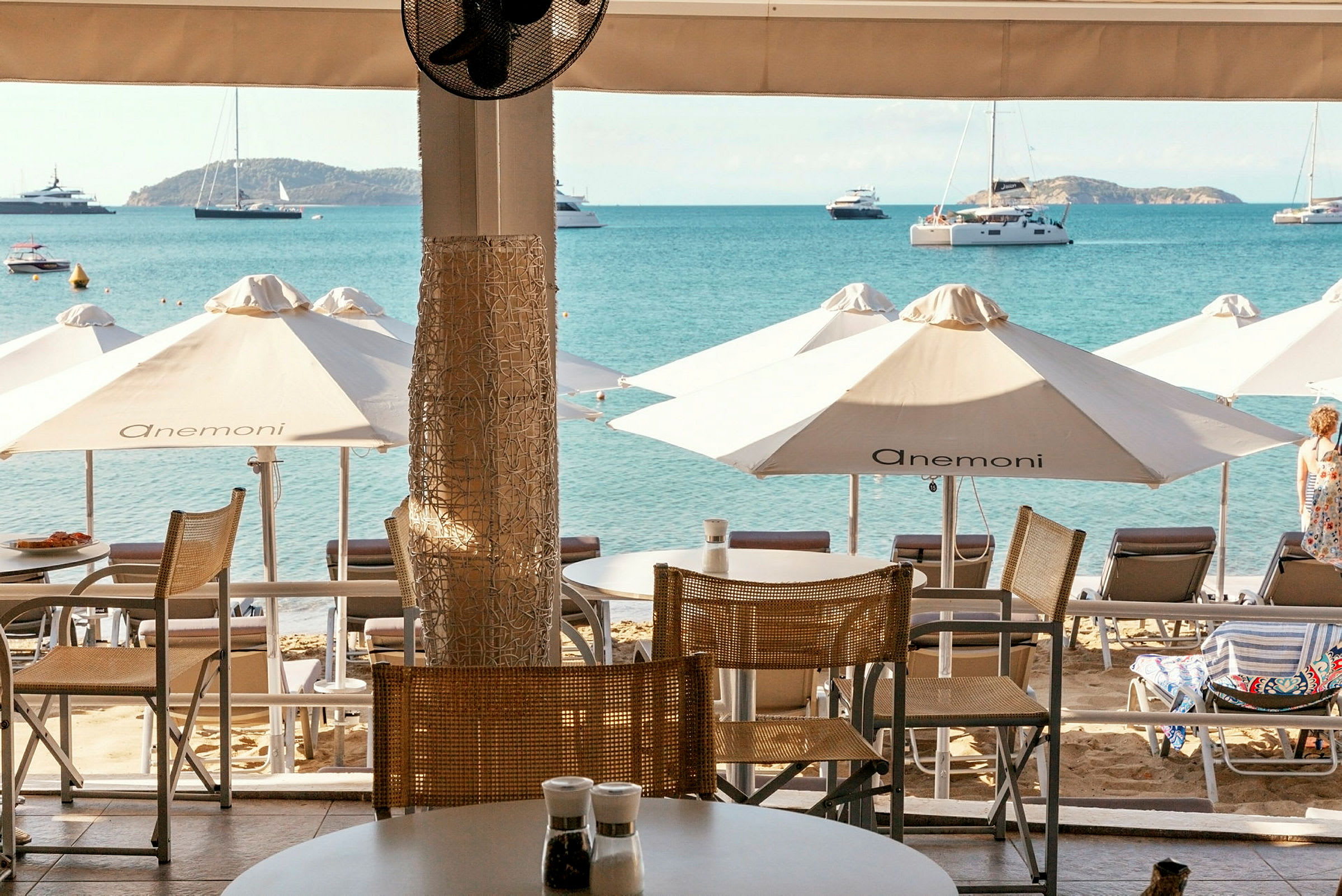 Utsikt från en terrass mot stranden med solstolar, parasoller och havet i bakgrunden. (AI-genererad text)