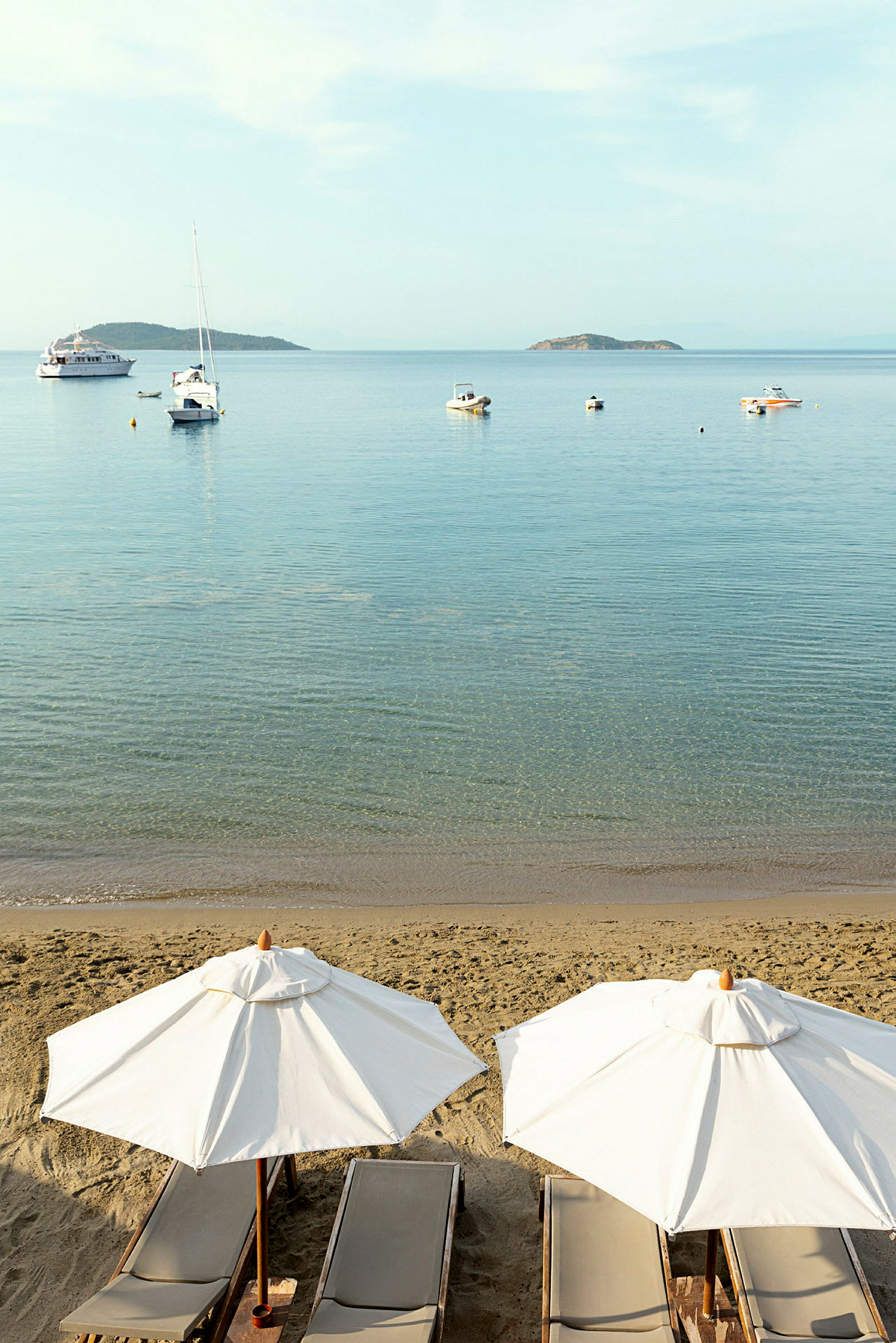 Strand med solstolar och parasoller, hav med båtar och öar i bakgrunden. (AI-genererad text)