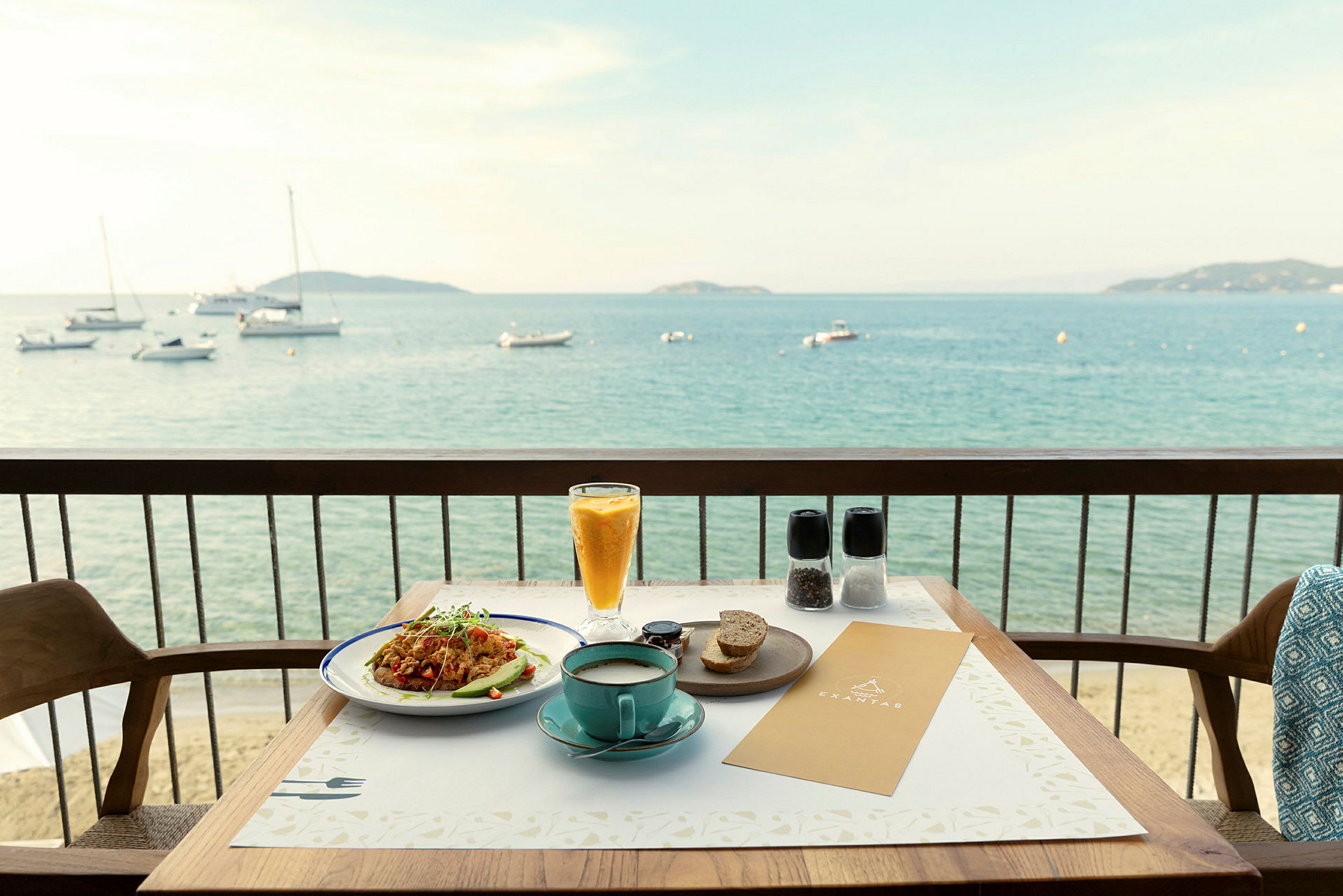 Utsikt över en tallrik med mat och en kopp kaffe placerade på ett bord med en balkong som vetter mot havet. (AI-genererad text)