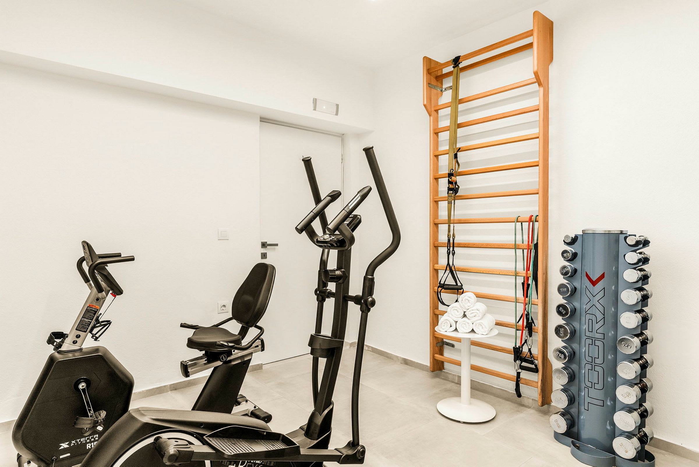 Ett gym med träningscykel, crosstrainer, ribbstol, och hantlar. (AI-genererad text)
