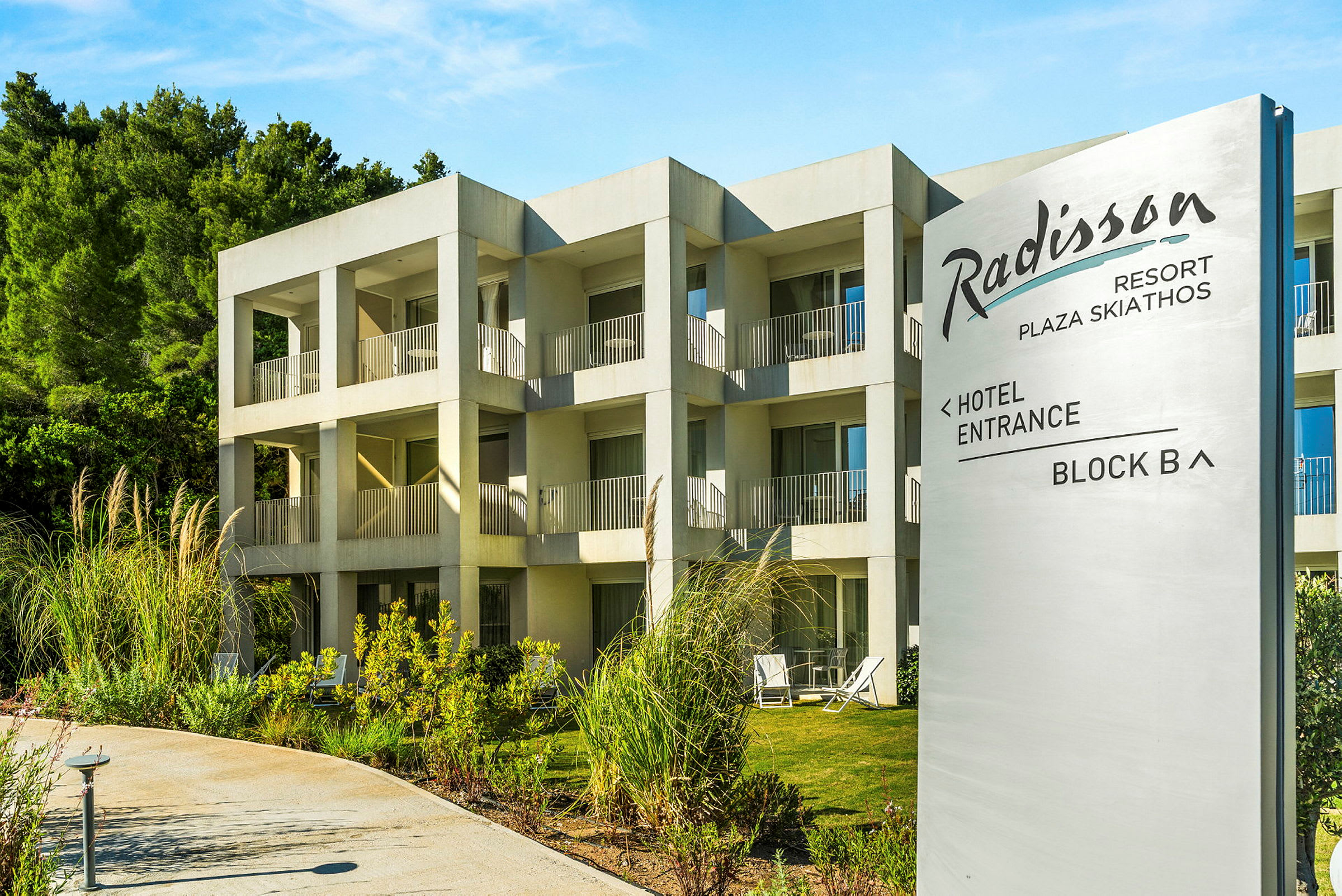 Hotellbyggnad med flera rum och balkonger, med en skylt som visar Radisson Resort Plaza Skiathos. (AI-genererad text)