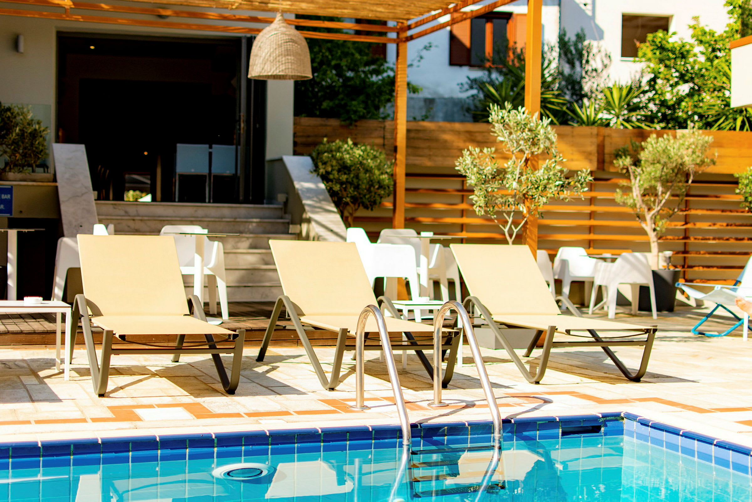Tre solstolar vid en pool med bord och stolar i bakgrunden. (AI-genererad text)