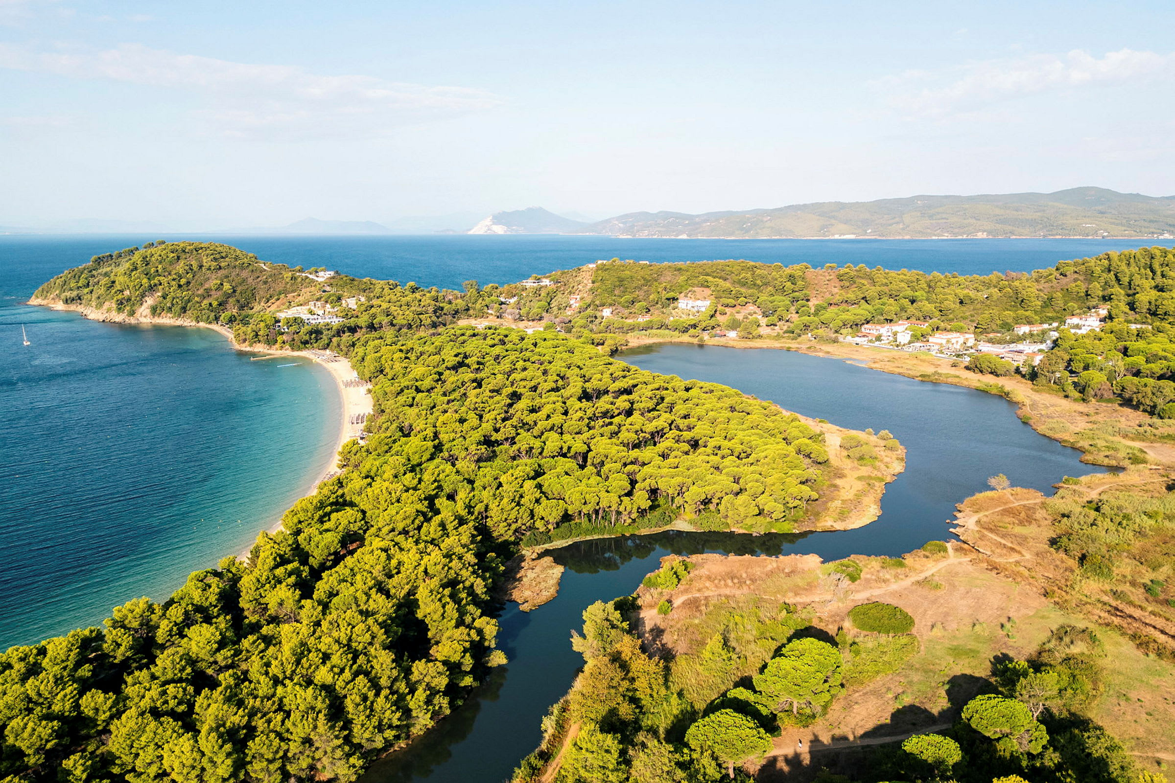 Flygfoto av en kustlinje med sandstrand, grönskande skog och lugnt vatten. (AI-genererad text)