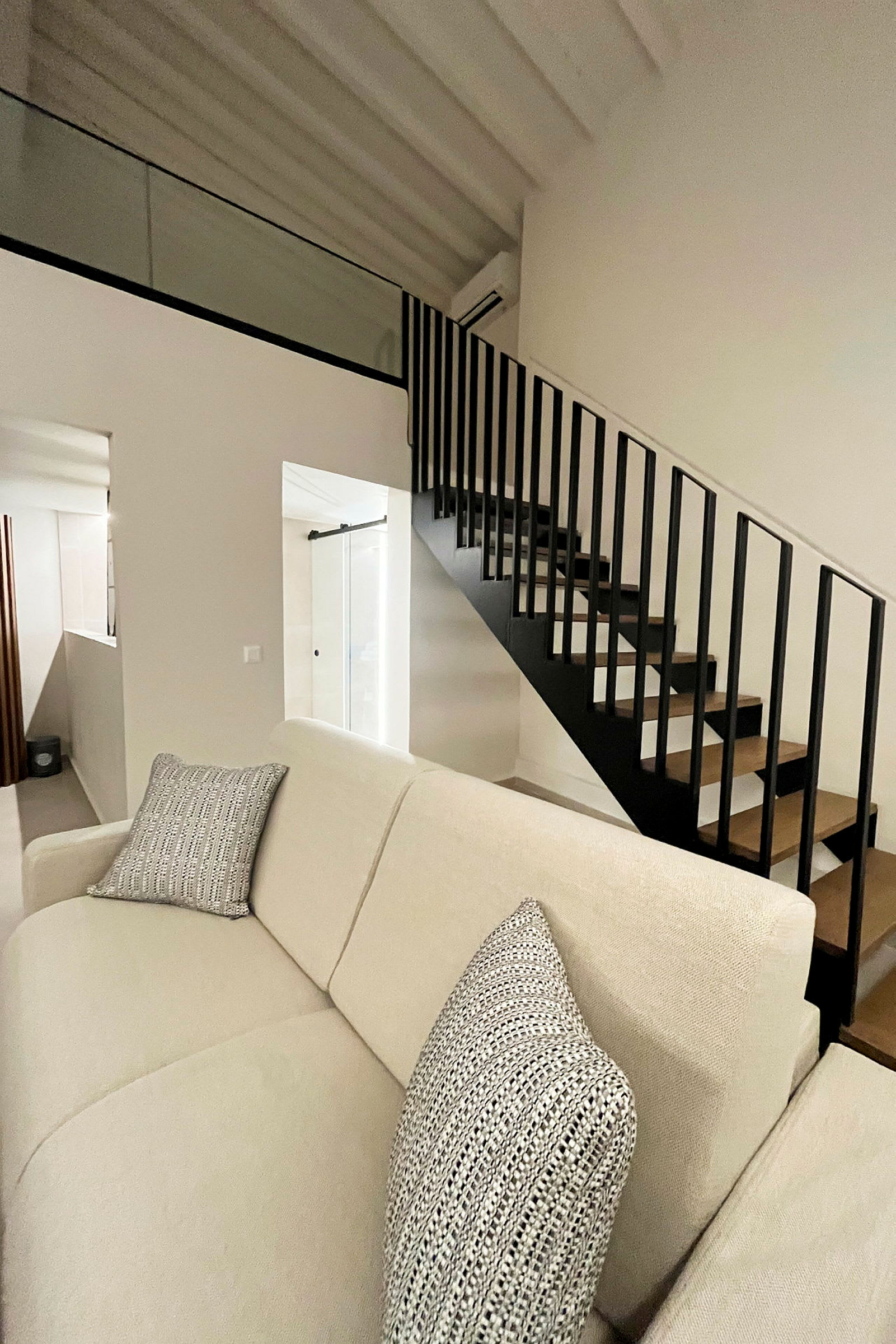 Bild på en modern inomhusmiljö med en ljus soffa med kuddar samt en svart trappa. (AI-genererad text)