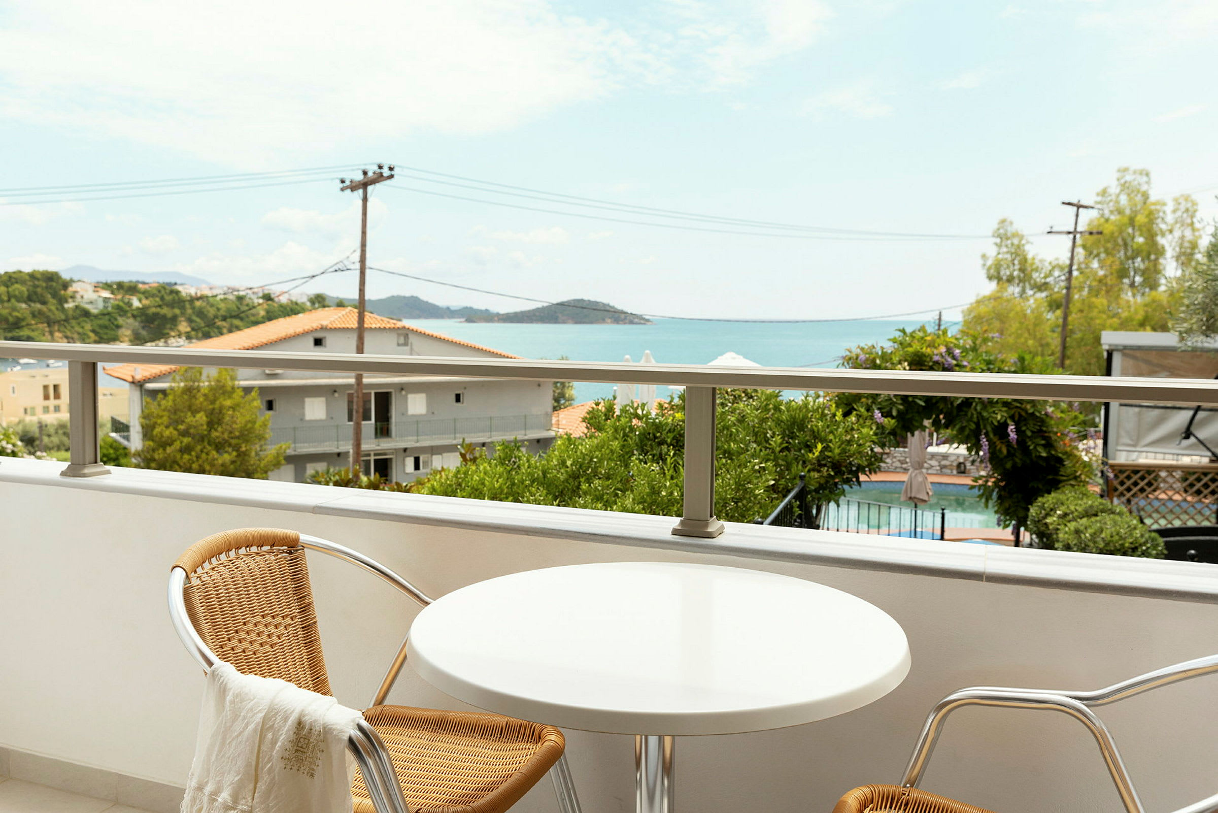 En balkong med ett litet bord och två stolar, med utsikt över en pool och havet. (AI-genererad text)
