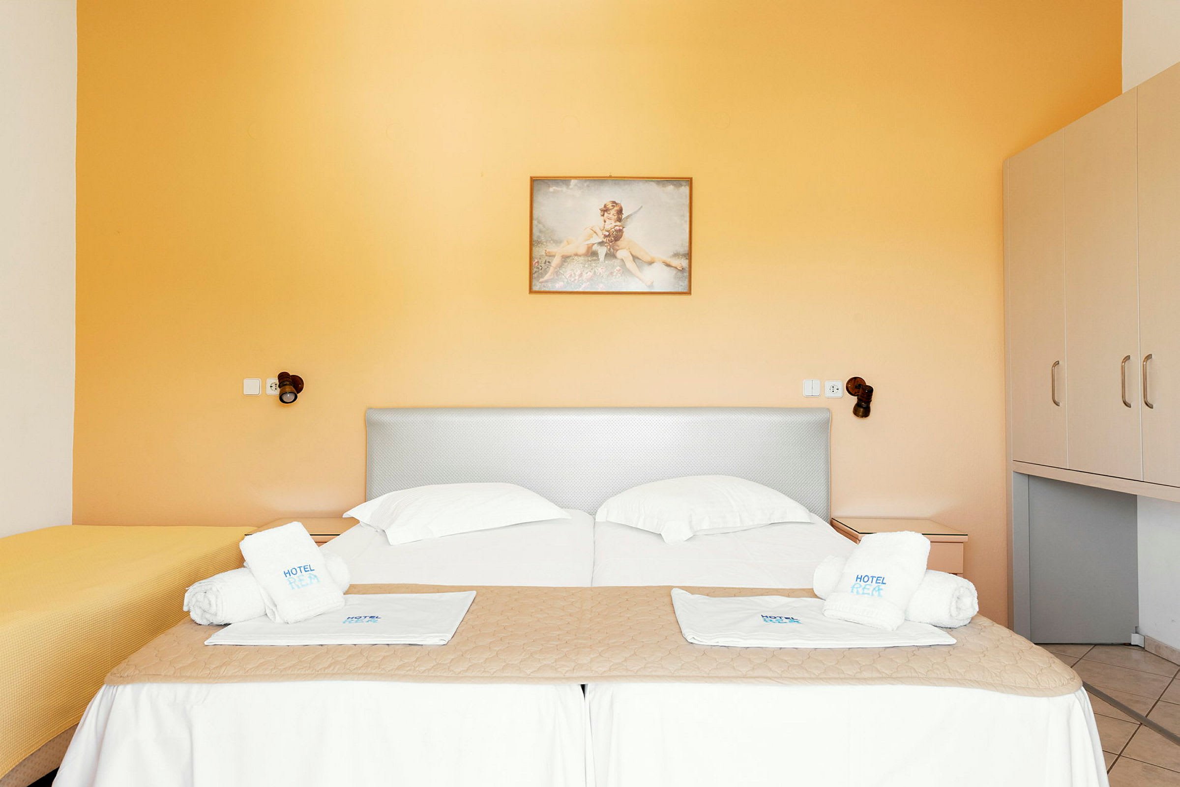 Ett hotellrum med två sängar klädda i vita sängkläder och handdukar placerade ovanpå. Väggarna är målade i orange färg. (AI-genererad text)