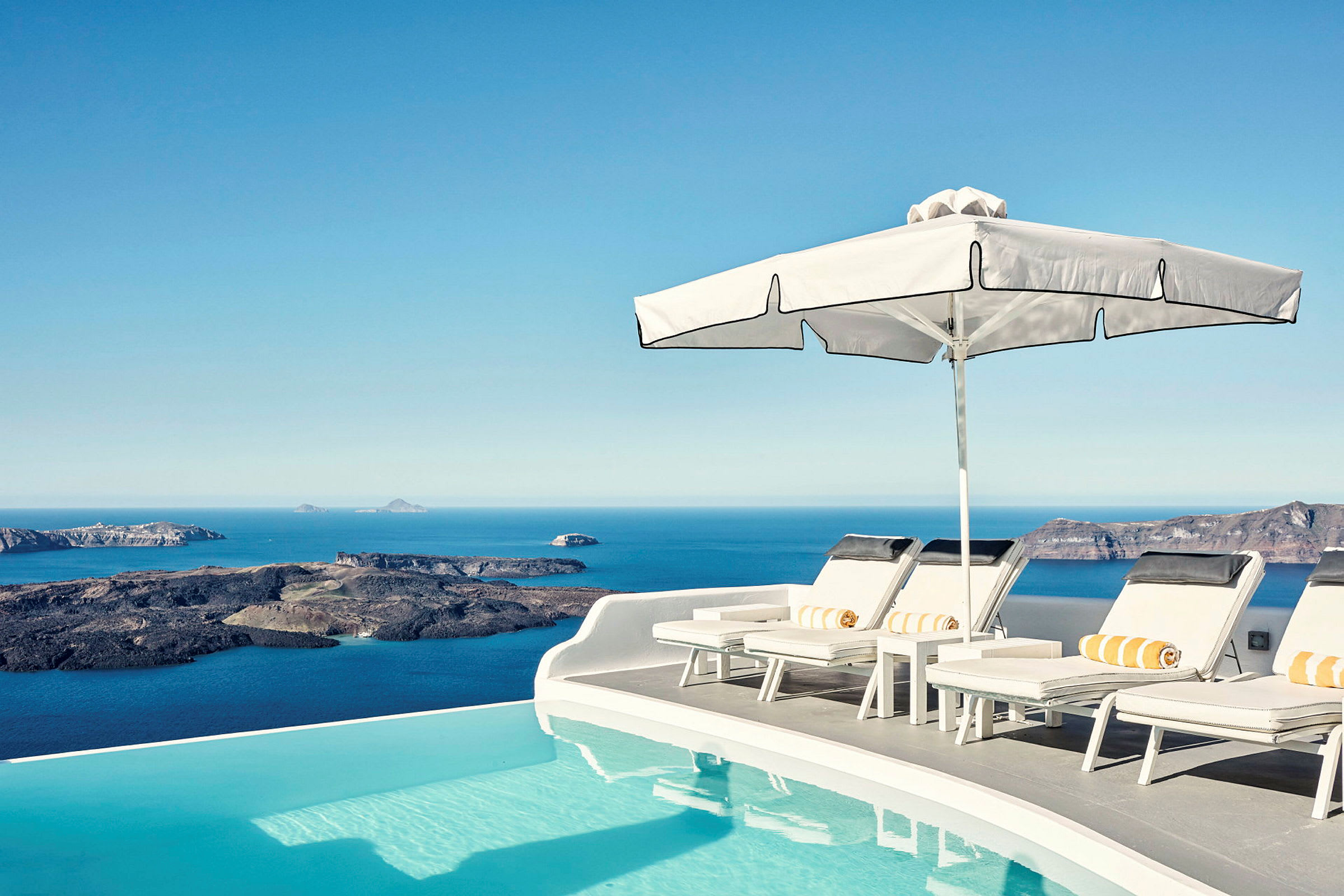 Soldäck vid en infinitypool med utsikt över havet och klippor i bakgrunden. (AI-genererad text)
