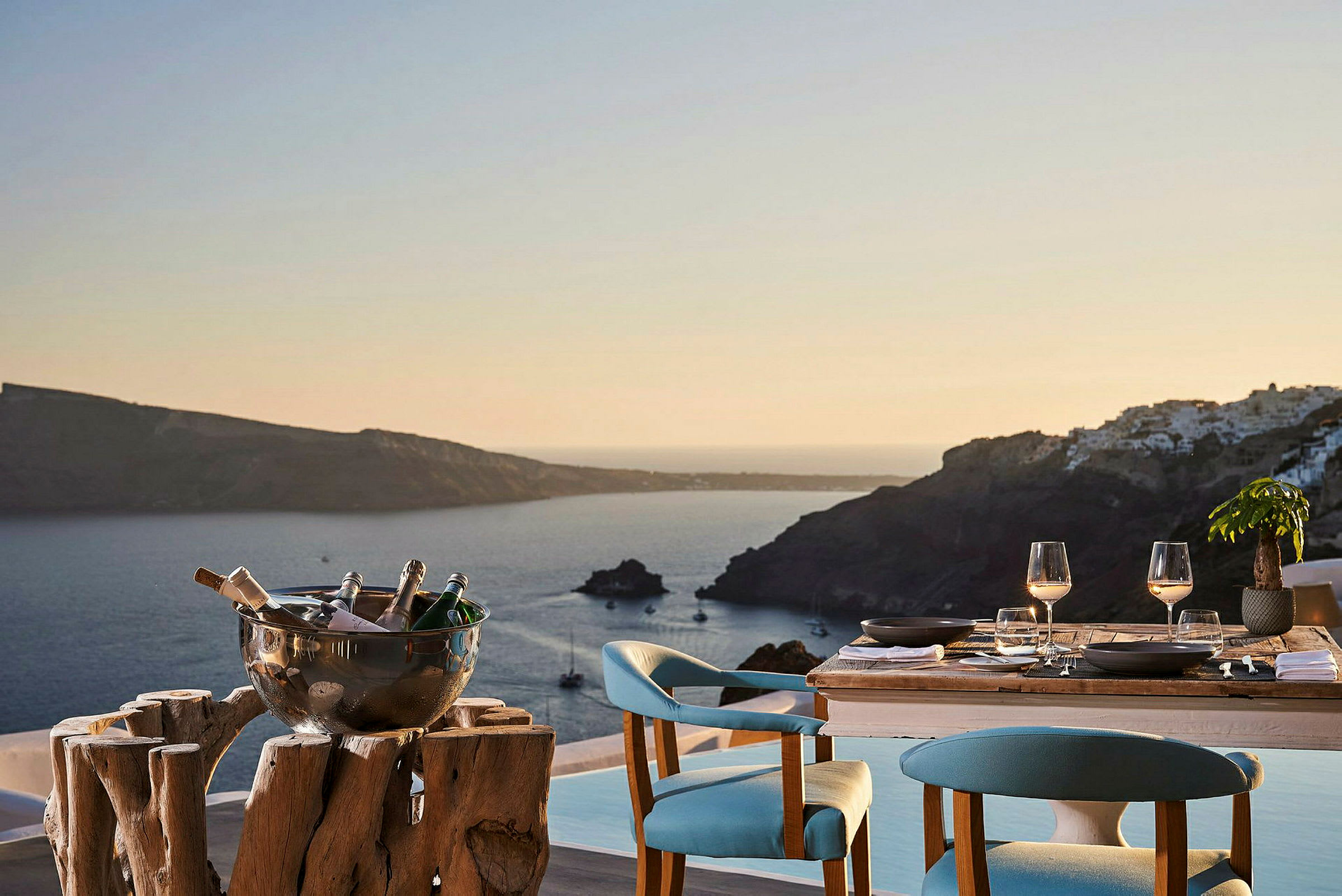Ett dukat bord med två sittplatser och en utsikt över havet och omkringliggande öar i solnedgång. (AI-genererad text)