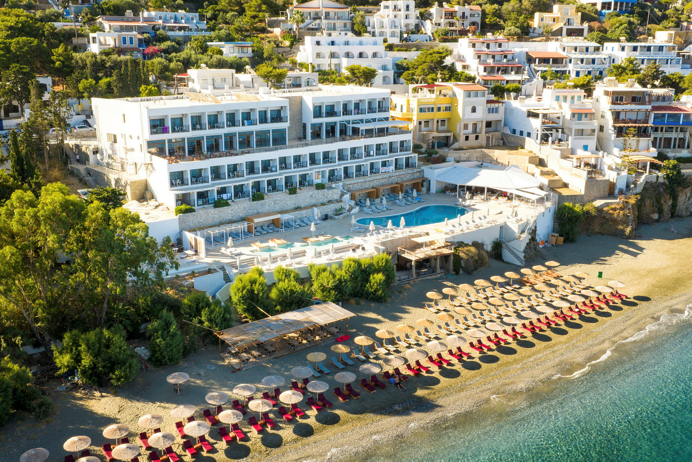 Hotellkomplex med poolområde och solstolar på en sandstrand. (AI-genererad text)