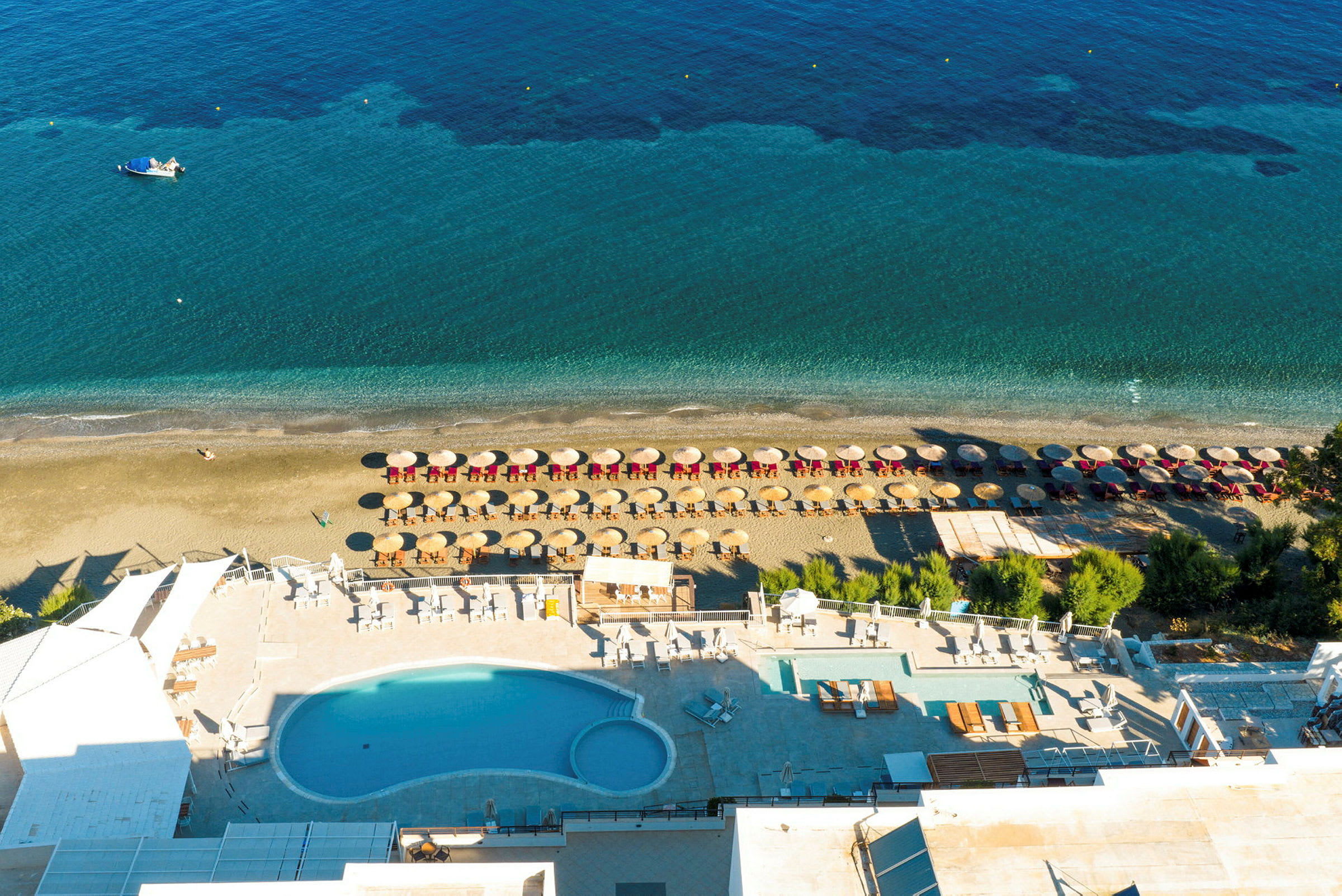 Fågelperspektiv av strand med parasoller och solstolar samt en pool i förgrunden. (AI-genererad text)
