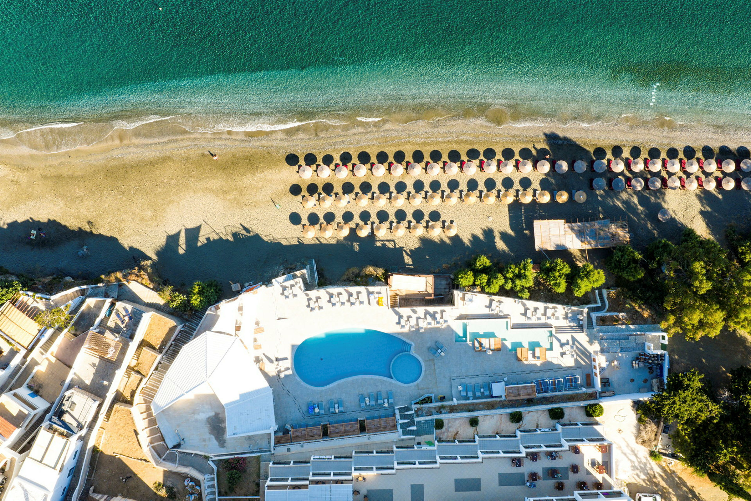 Flygbild av hotellområde med pool och strand med solparasoller. (AI-genererad text)