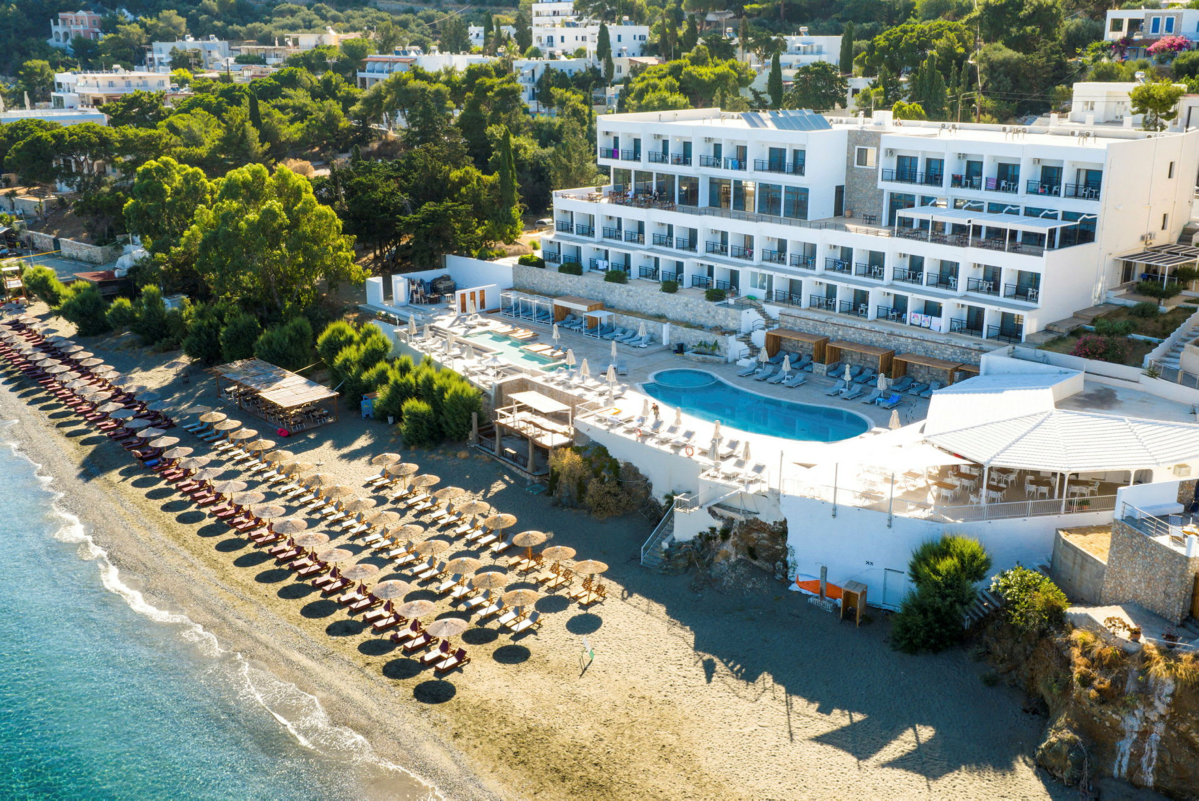 Vy över hotell vid stranden med pool och solsängar. (AI-genererad text)