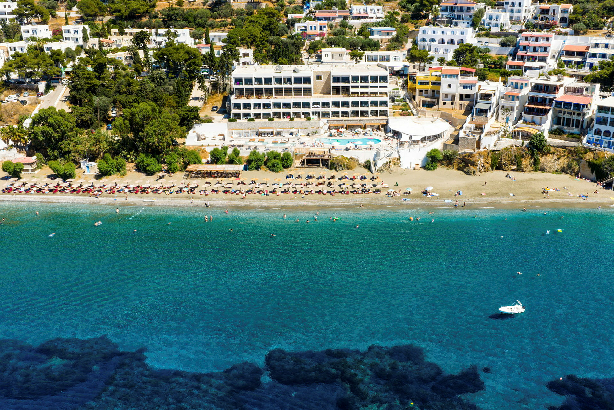 Bild av ett hotellkomplex med swimmingpool nära en strand med solstolar och parasoller. (AI-genererad text)