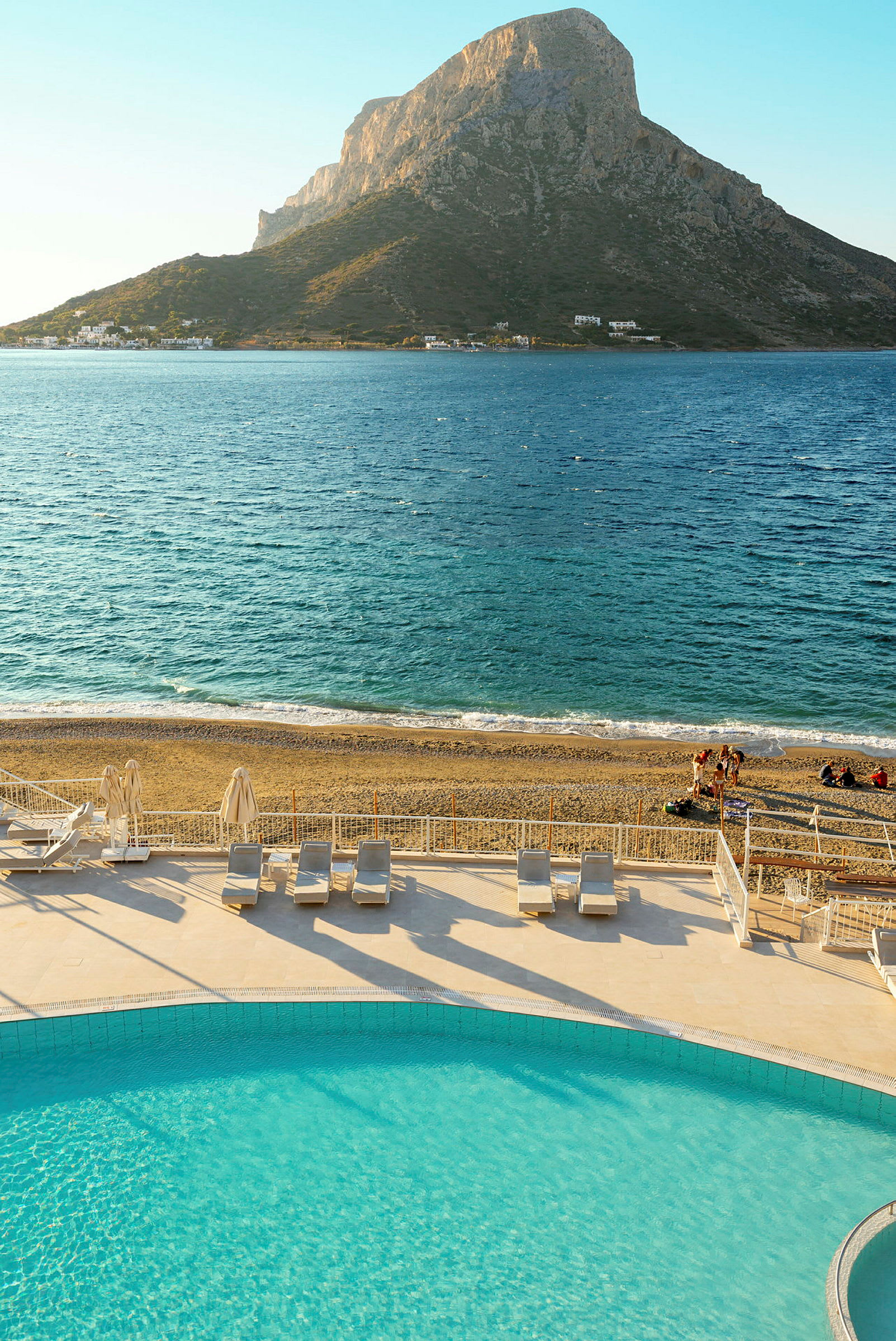 Bild av en pool, strand och hav med ett berg i bakgrunden. (AI-genererad text)