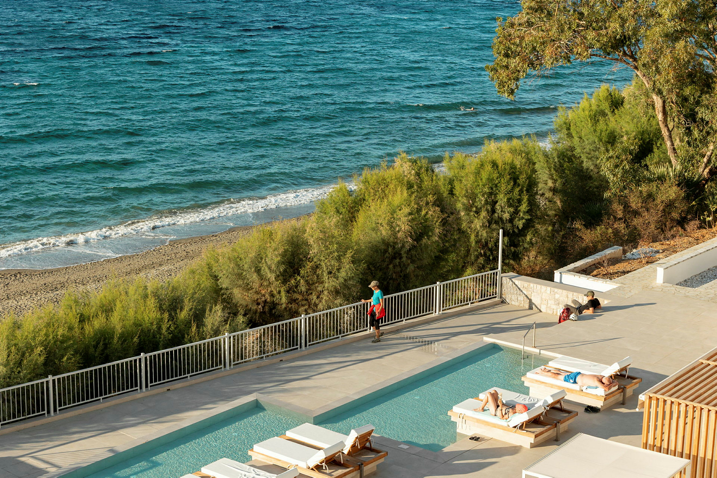 En utomhuspool med solstolar framför en sandstrand och havet. (AI-genererad text)