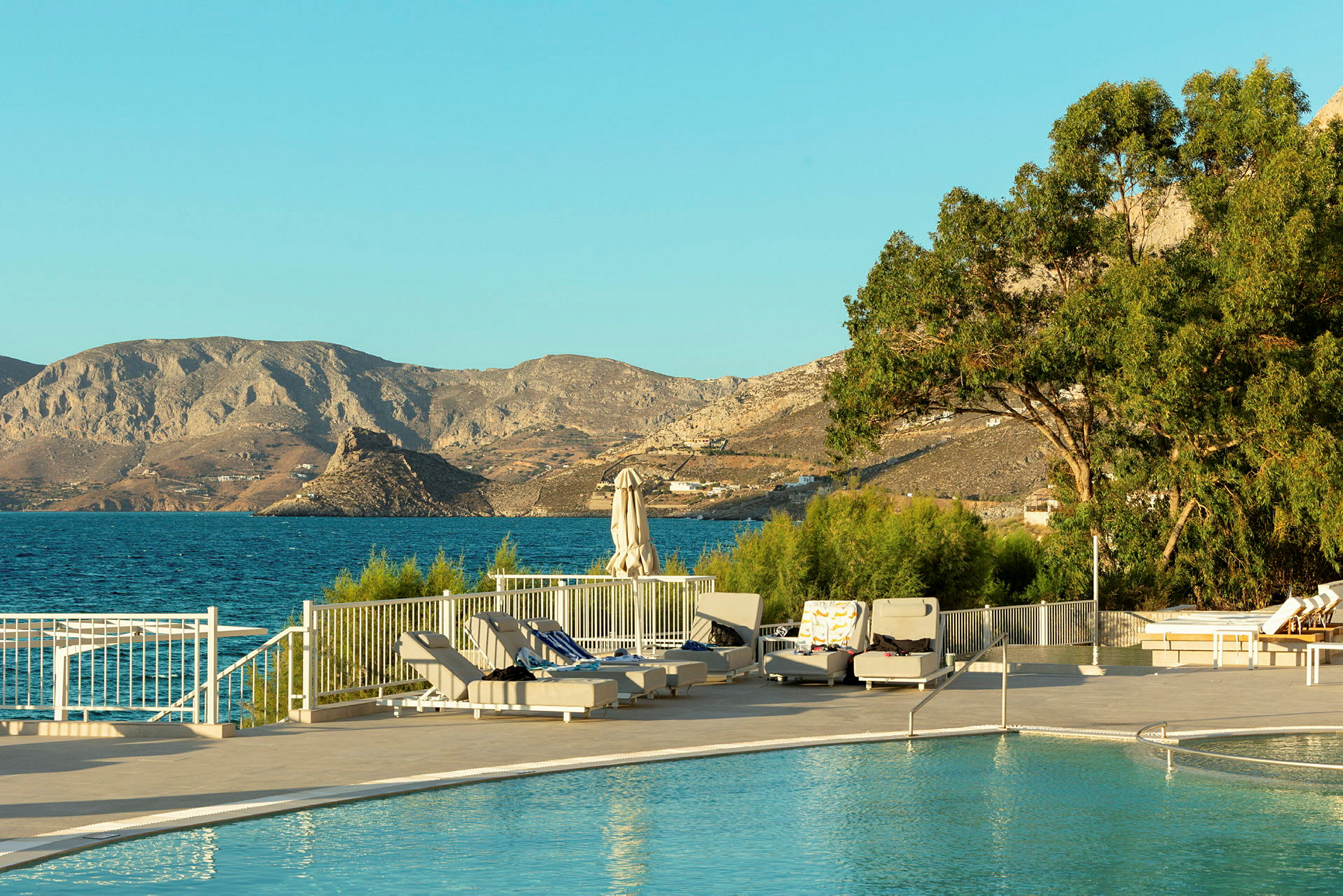 En pool med solstolar vid en kust med utsikt över bergen. (AI-genererad text)