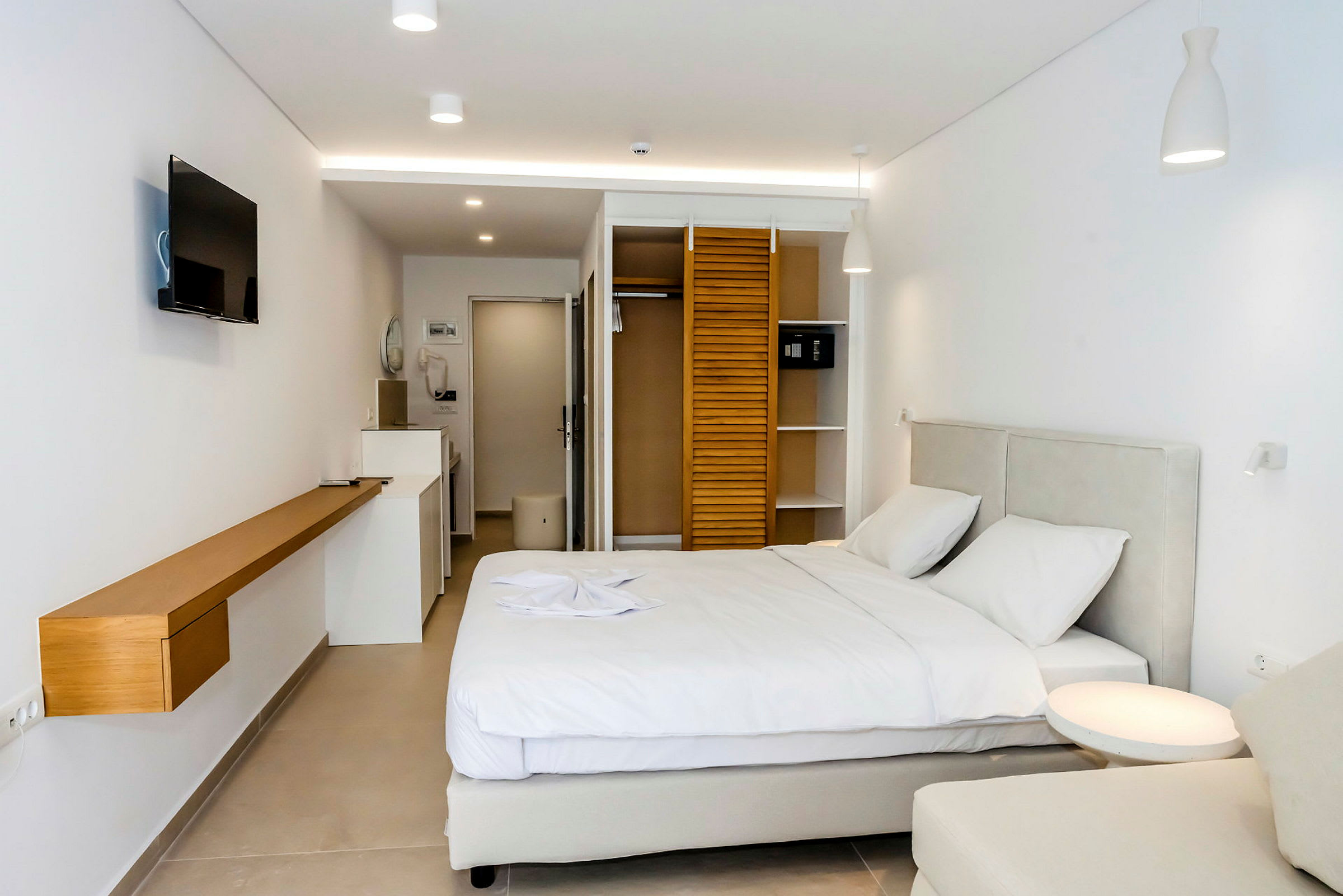 Hotellrum med en dubbelsäng, en TV på väggen och hyllor vid garderoben. (AI-genererad text)