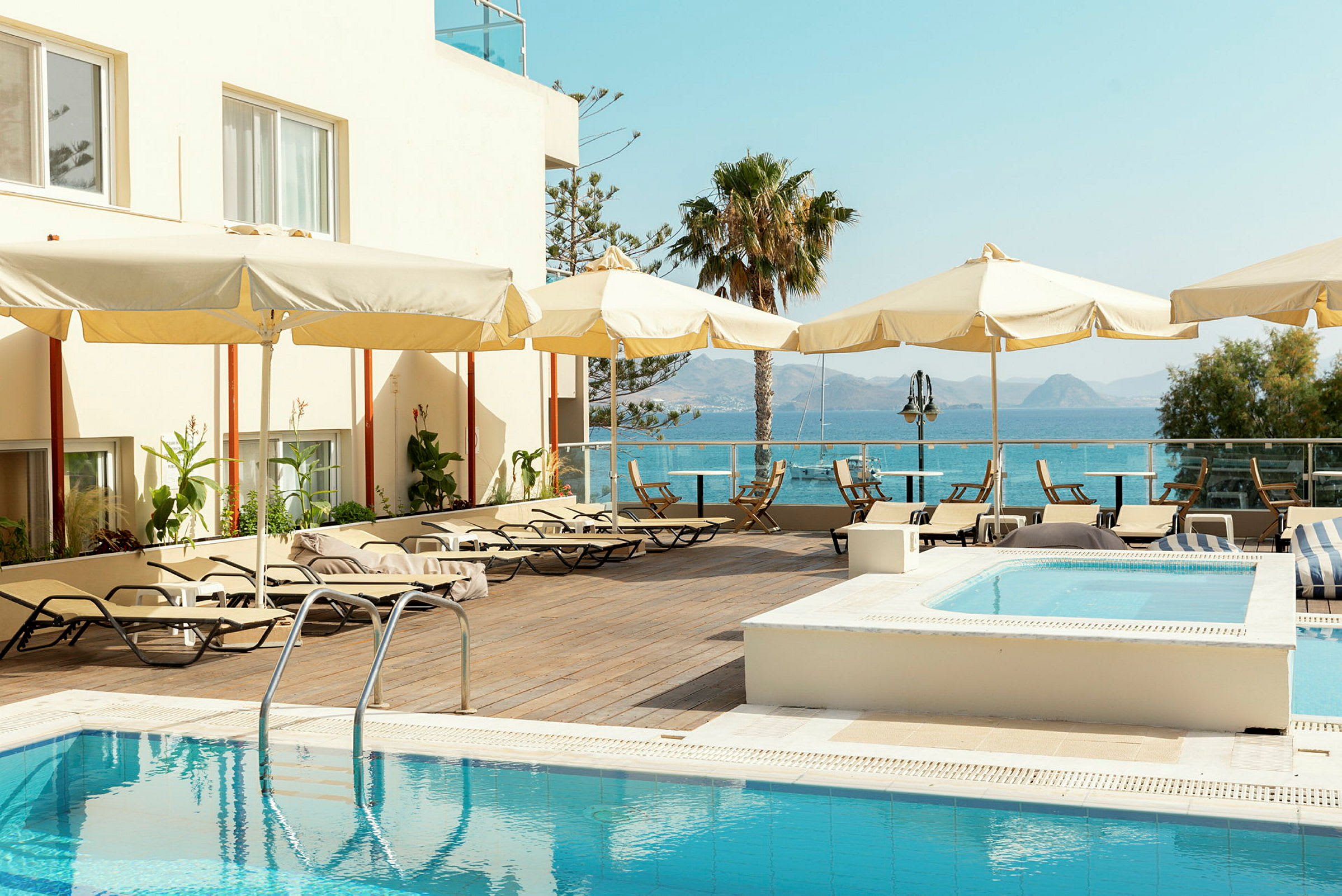 Poolområde vid hotell med solsängar och parasoller, havet och berg i bakgrunden. (AI-genererad text)