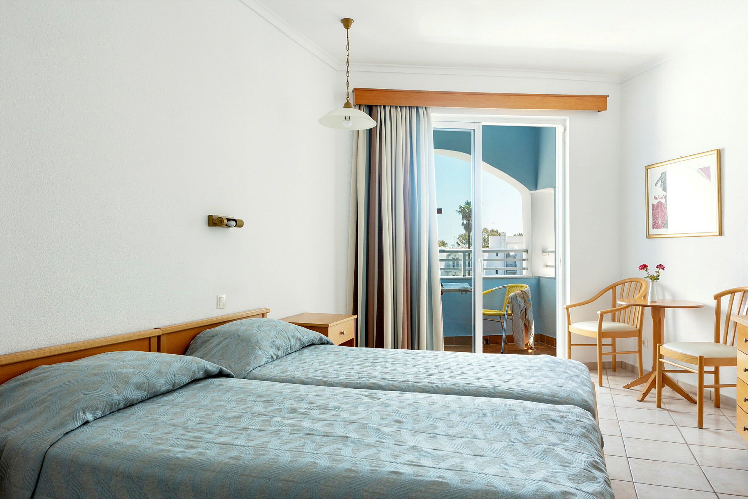 Ett hotellrum med två enkelsängar, ett bord med två stolar och en balkong med utsikt. (AI-genererad text)