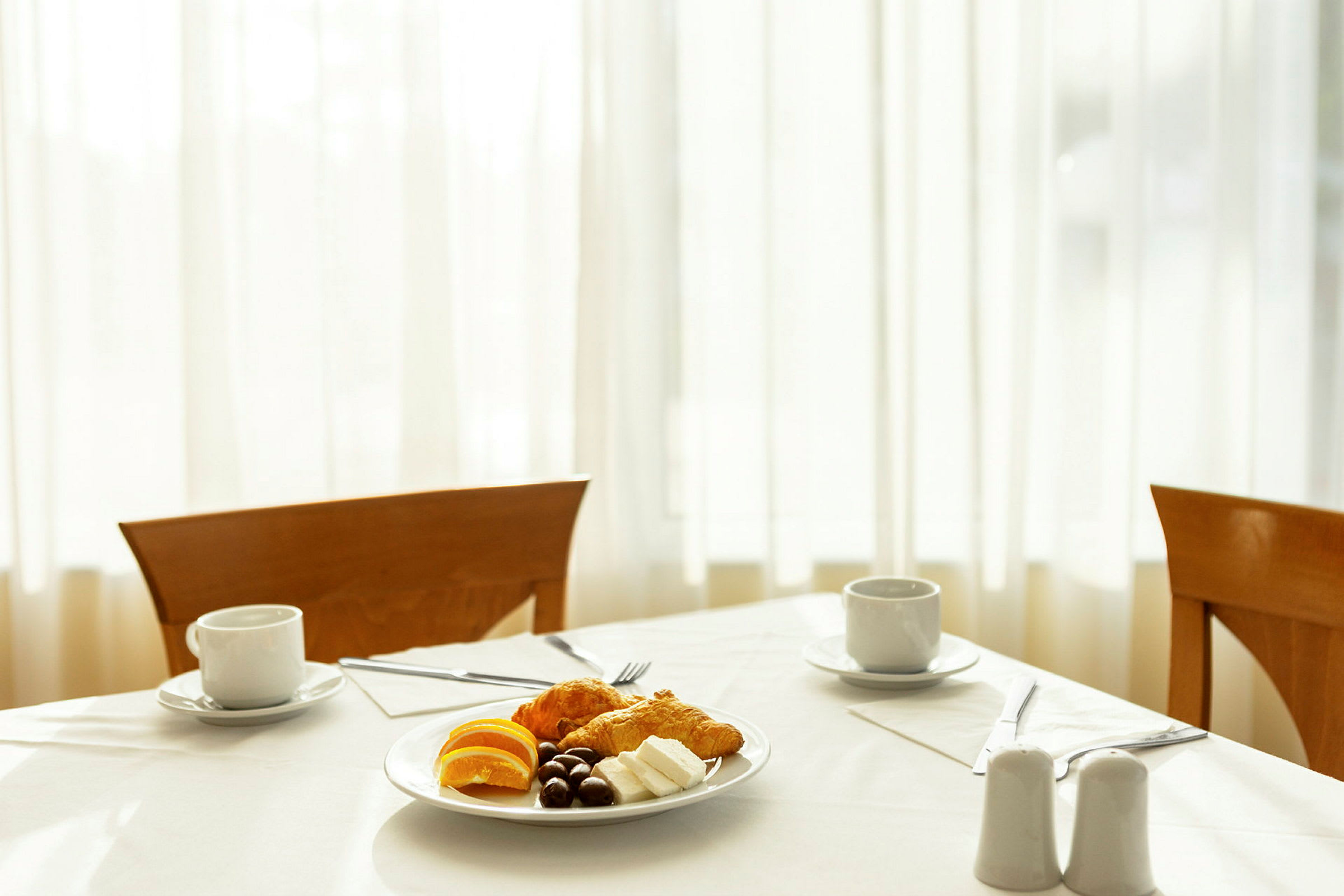En dukad frukost med ett fat innehållande croissanter, apelsinskivor, ost och choklad samt två koppar kaffe. (AI-genererad text)