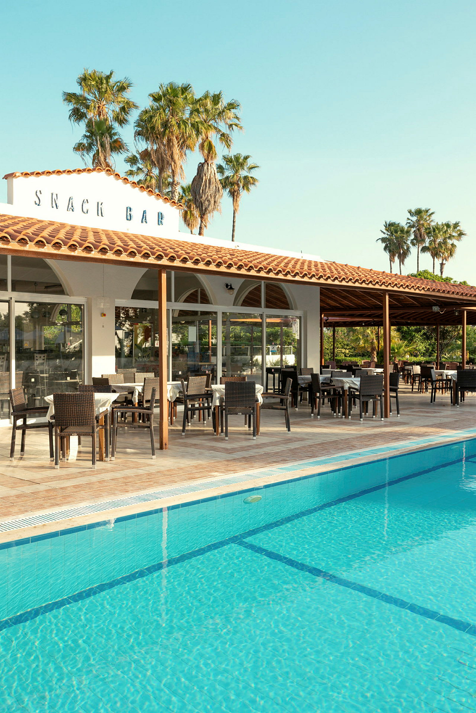 Poolområde med sittplatser vid en snackbar. (AI-genererad text)