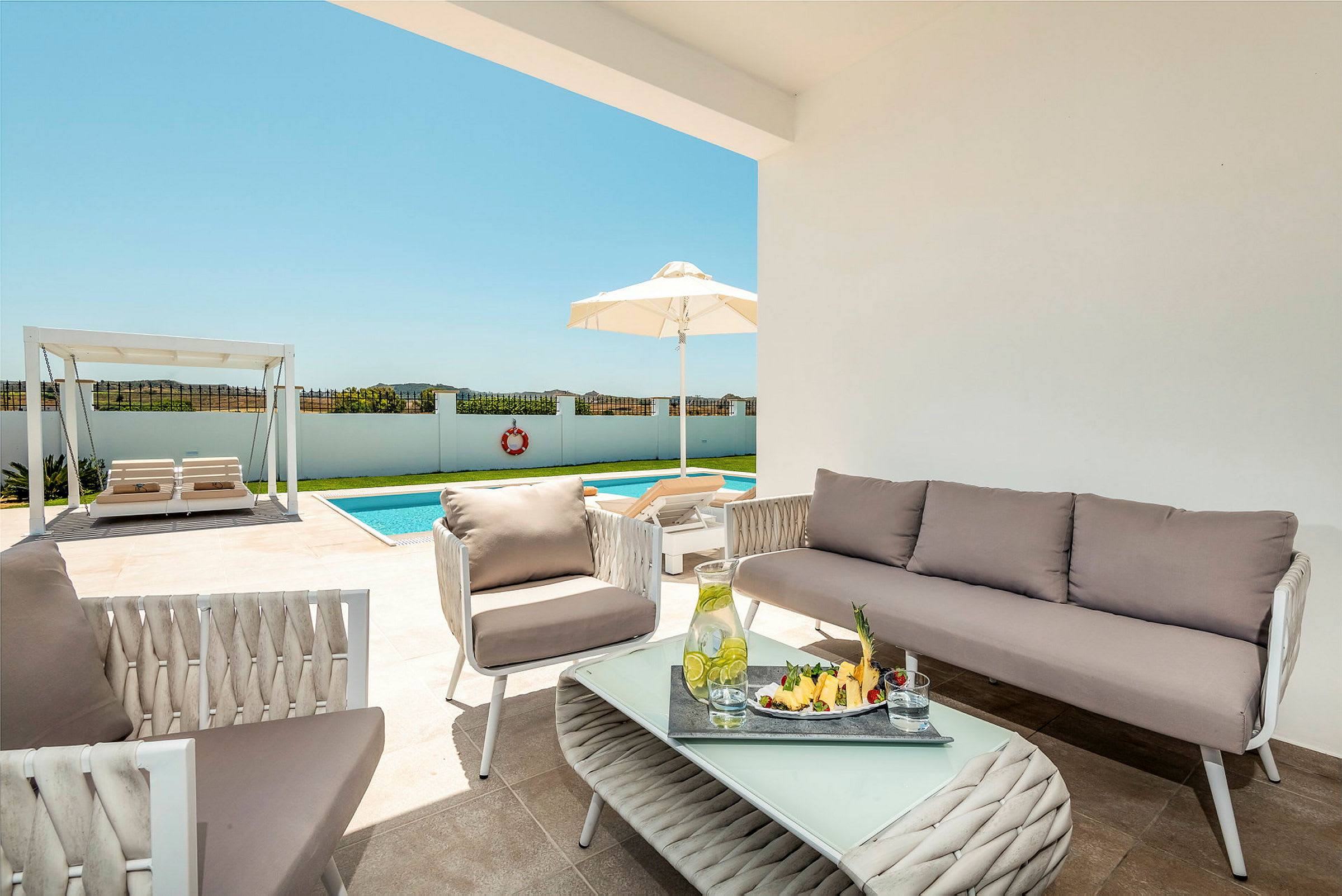 Bild av en terrass med utomhusmöbler, en pool och en pergola i bakgrunden. (AI-genererad text)