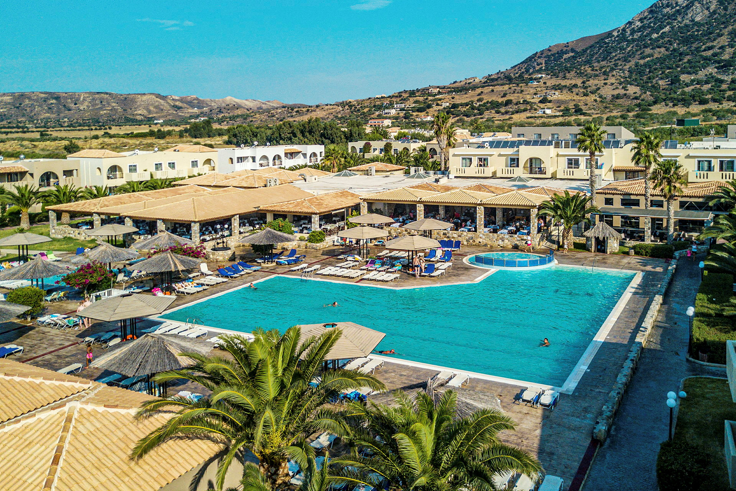 Hotellområde med pool, solstolar och parasoller. Byggnader i bakgrunden. (AI-genererad text)