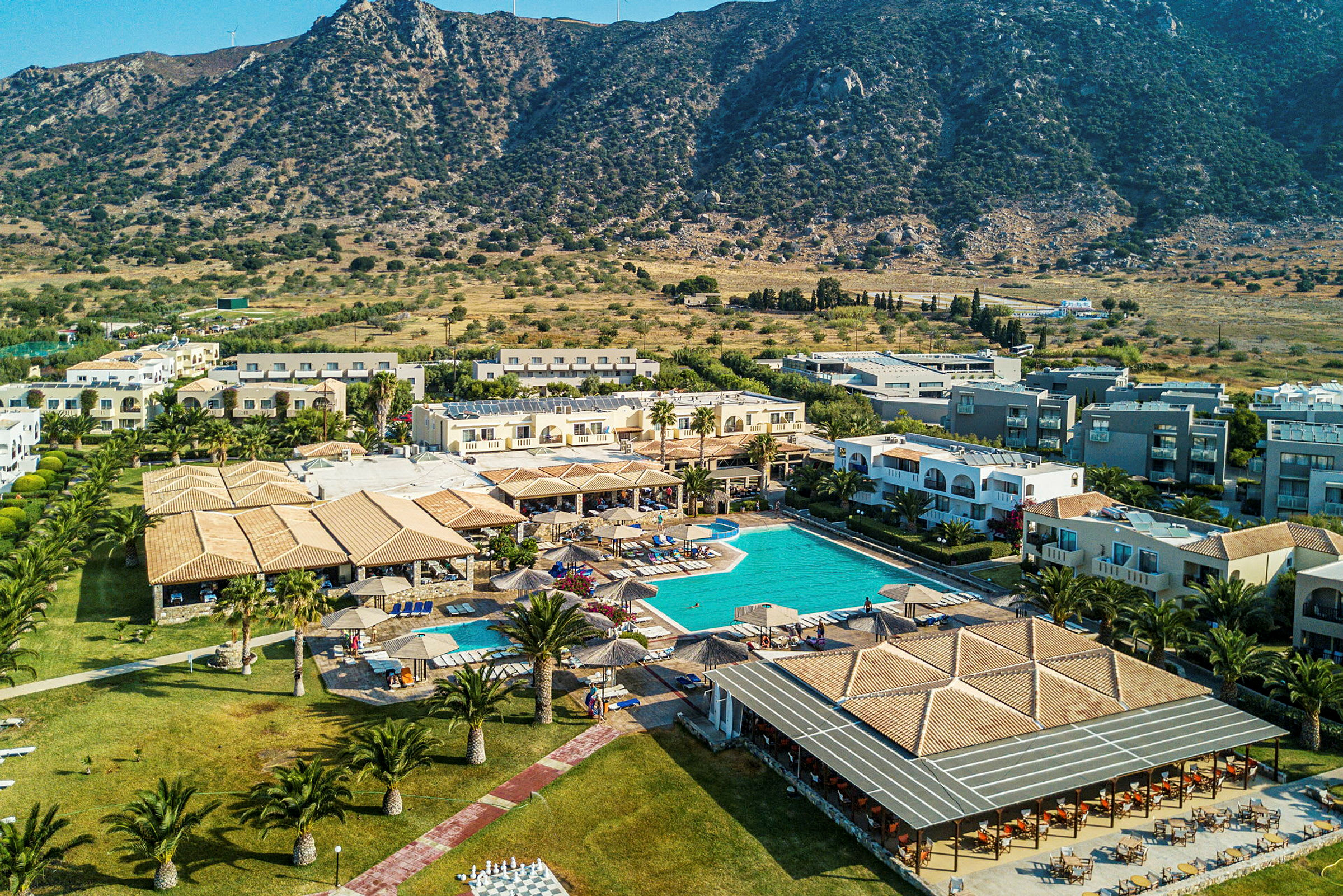 Bild av ett semesterhotell med pool och omgivande byggnader, beläget nära en bergig landskap. (AI-genererad text)