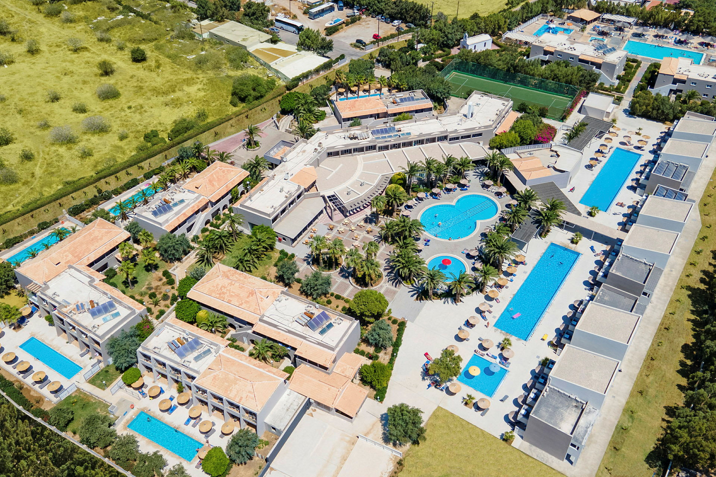 Flygfoto av en semesteranläggning med swimmingpooler, byggnader och palmer. (AI-genererad text)