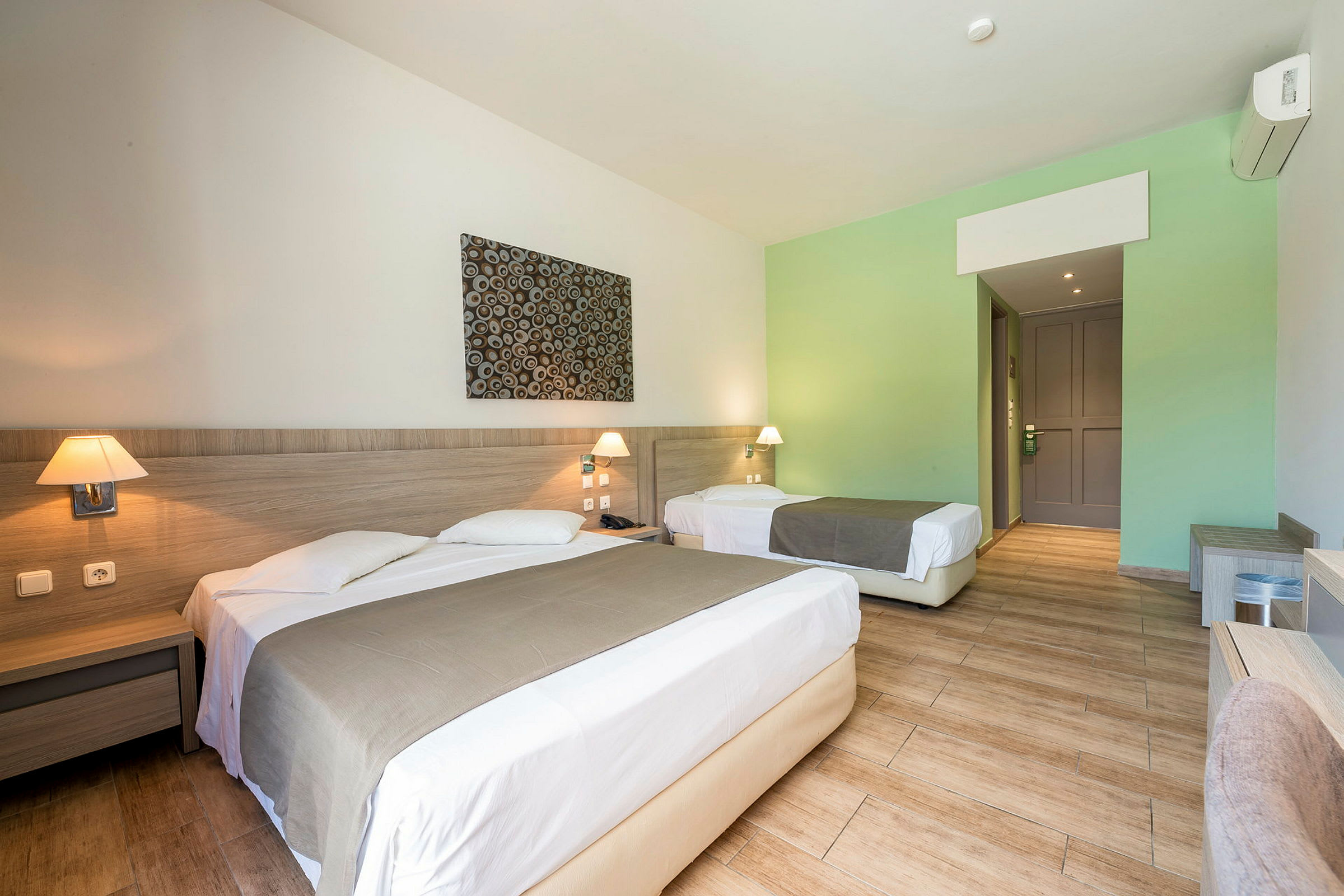 Hotellrum med en dubbelsäng och en enkelsäng, båda med överkast och nattygsbord. (AI-genererad text)