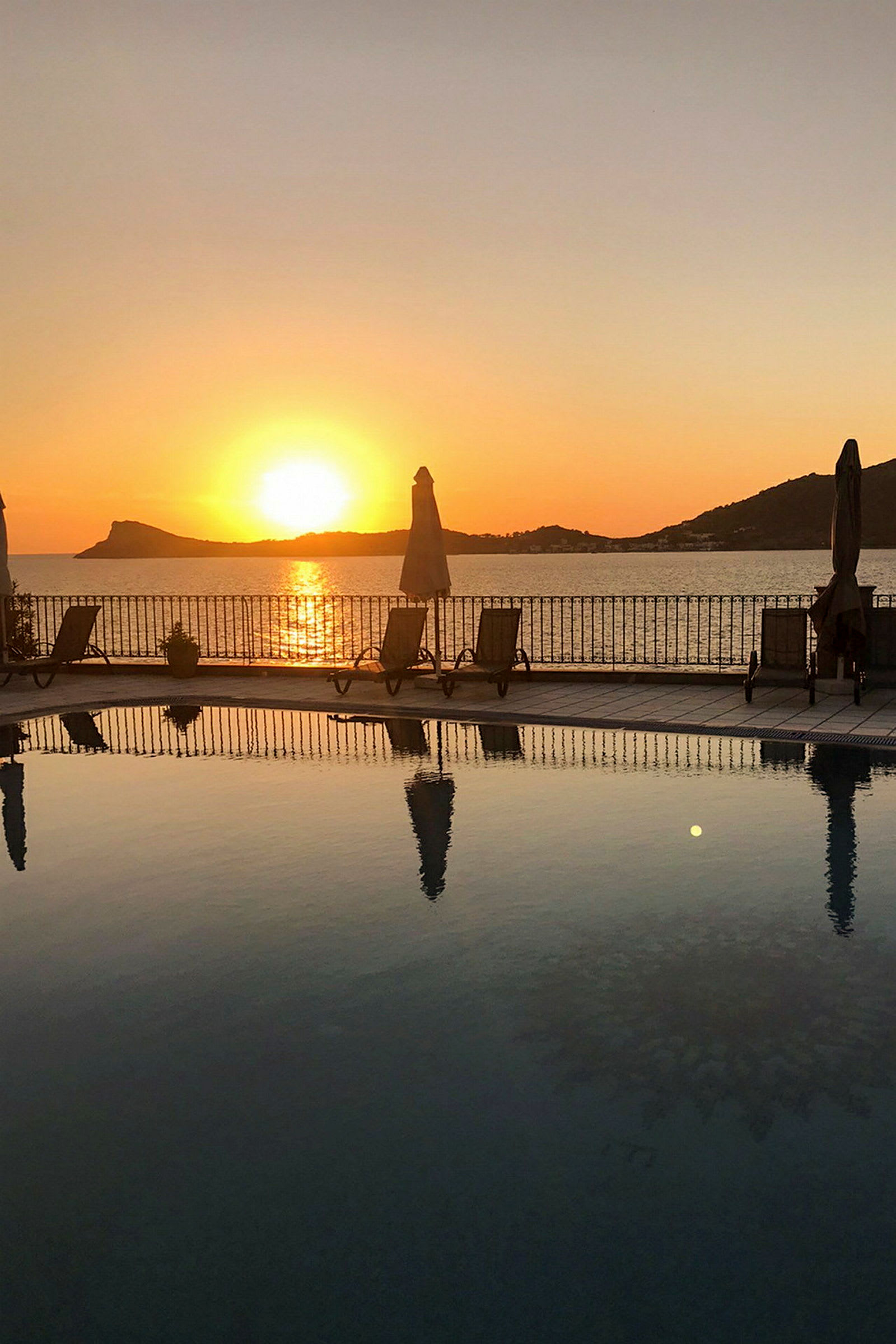 En solnedgång över havet med en pool och solstolar i förgrunden. (AI-genererad text)