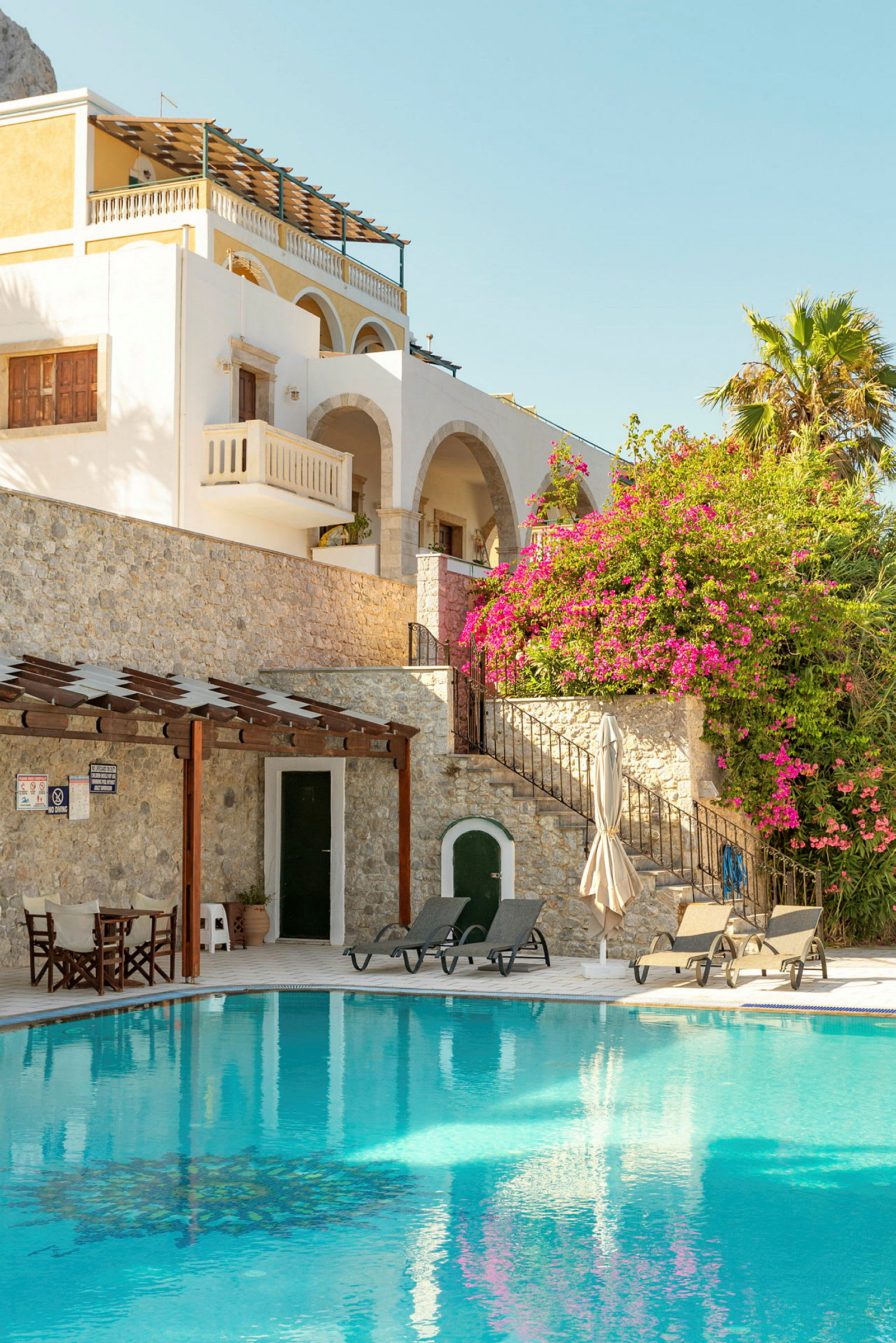 Bild av en pool framför en byggnad med stenfasad och bougainvillea. (AI-genererad text)