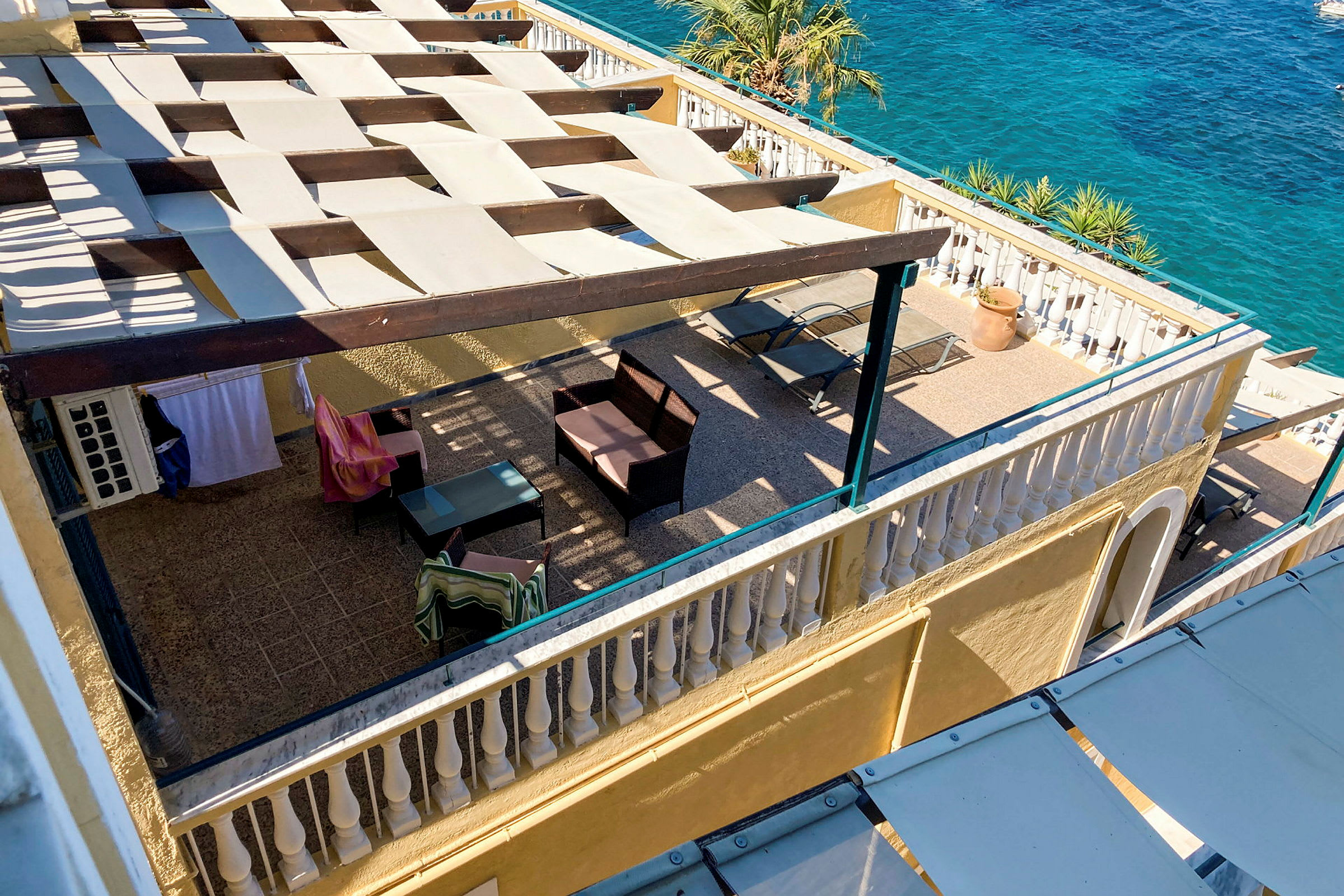 En vy över en terrasse med skuggande pergola, möbler och en utsikt mot havet. (AI-genererad text)