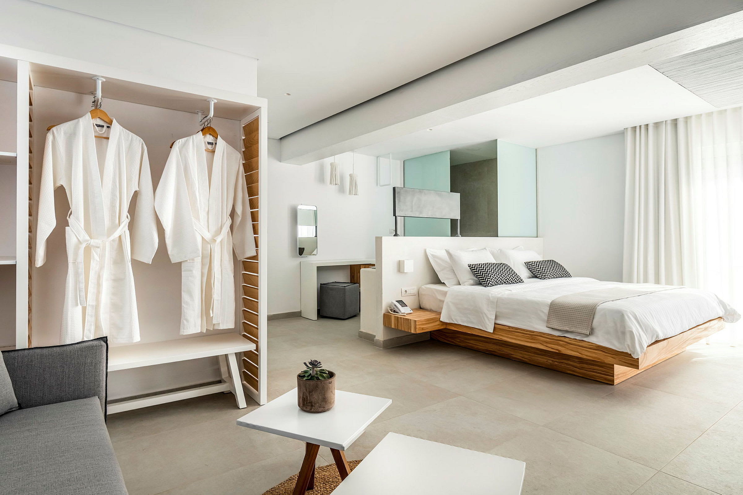 Bild av ett elegant hotellrum med en stor säng, vita badrockar hängande i en garderob och ljusa moderna möbler. (AI-genererad text)