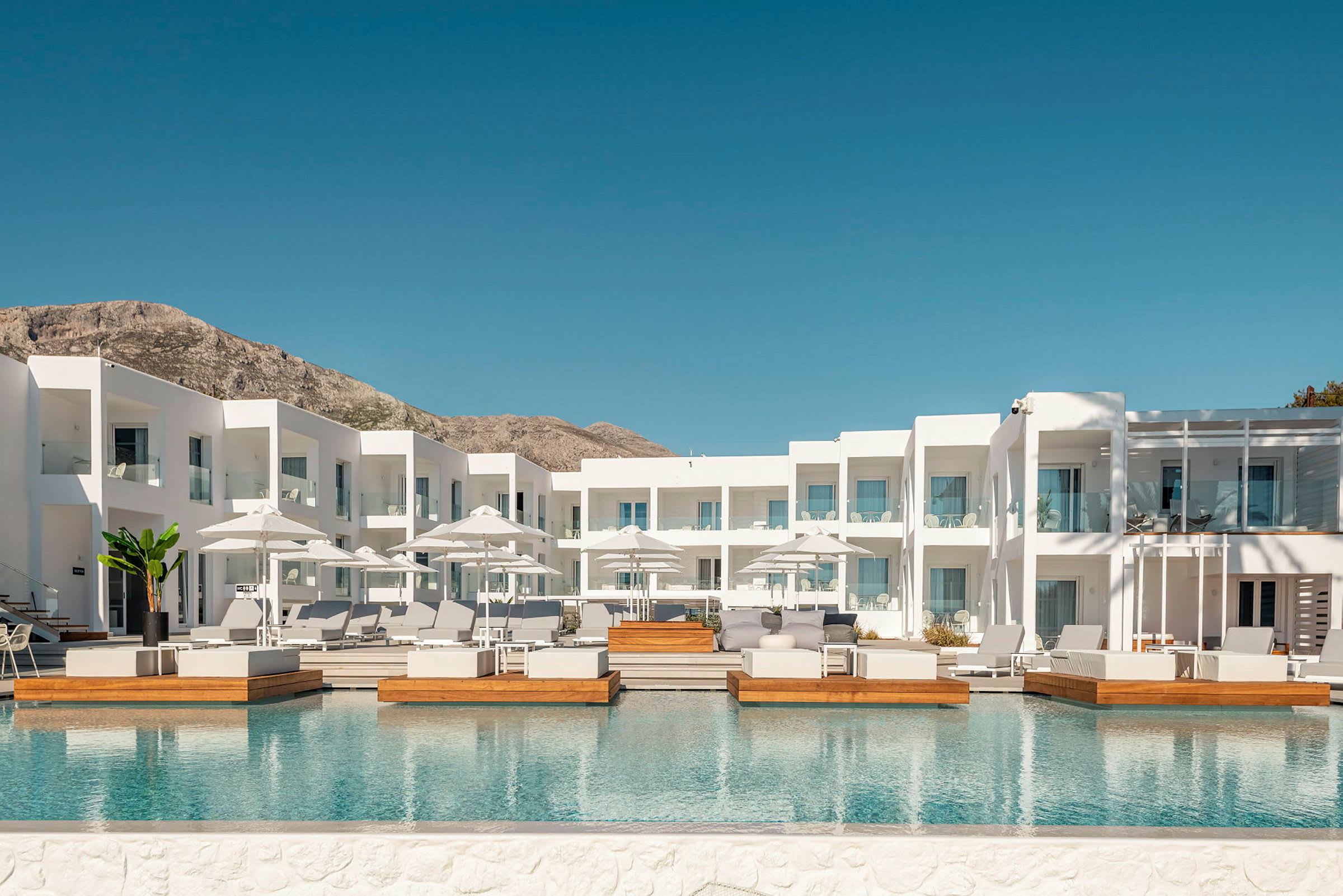 Vit hotellbyggnad med utomhuspool och solstolar. (AI-genererad text)