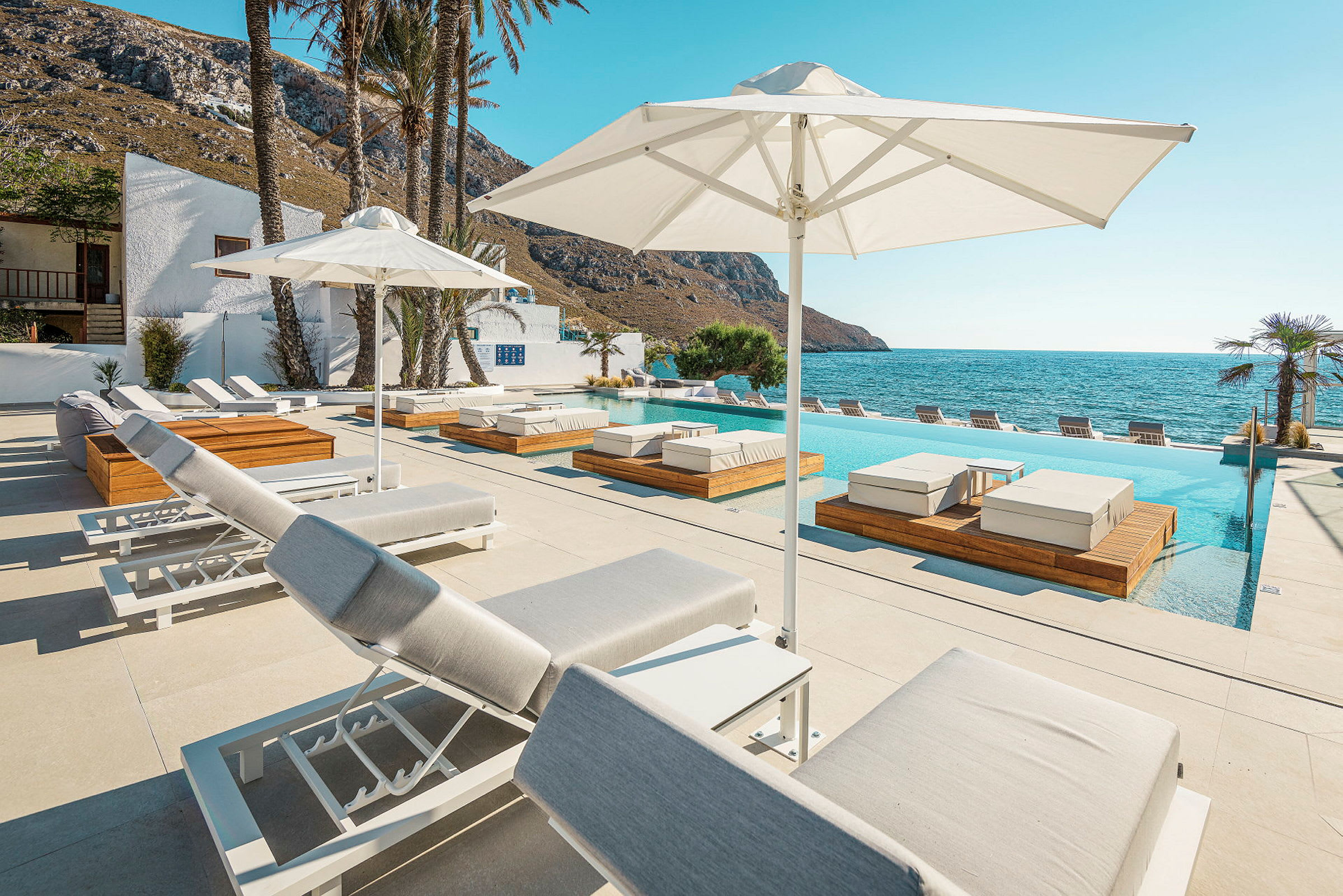 En bild av en utomhus swimmingpool nära havet med solstolar och parasoller. (AI-genererad text)