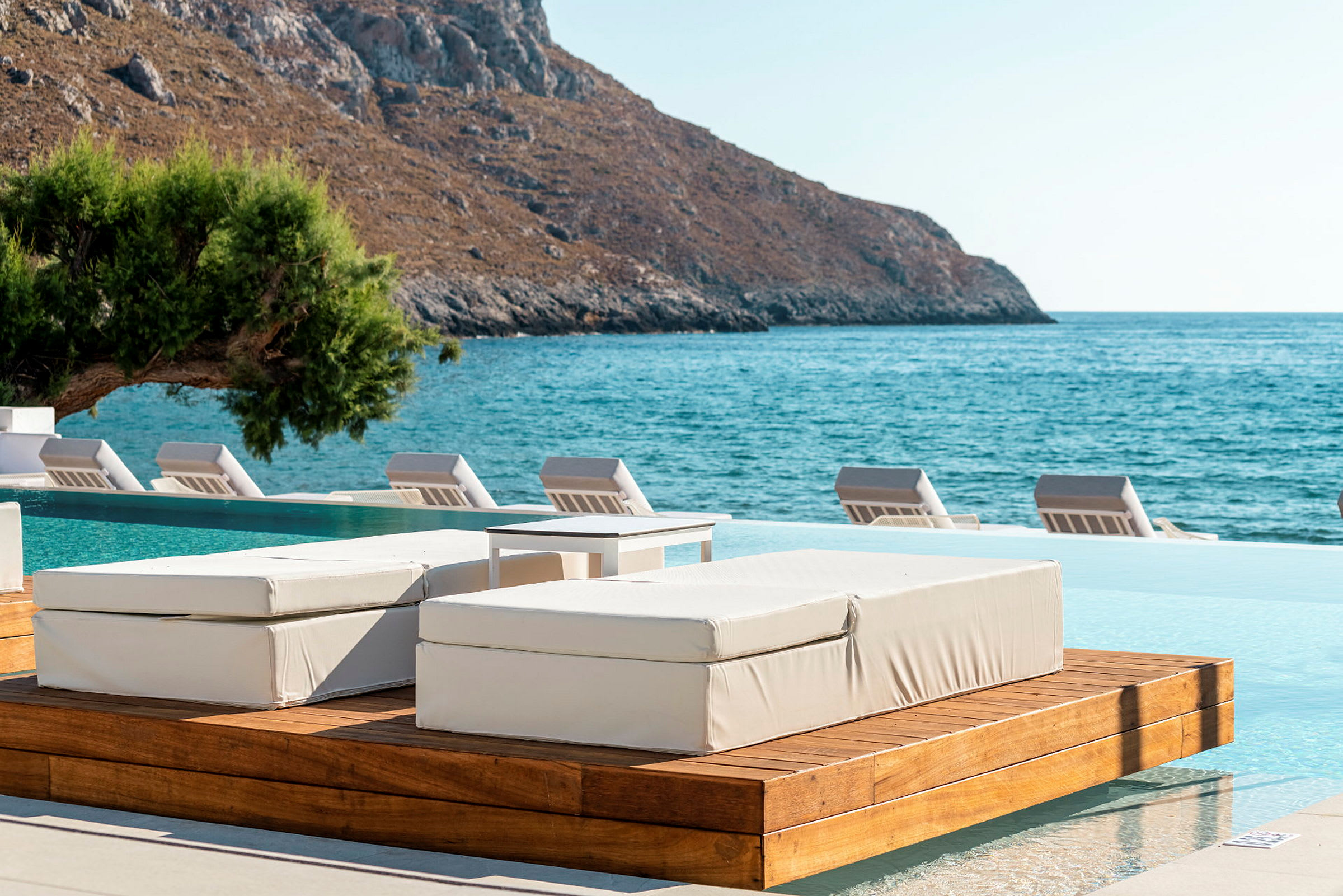 Bild av en infinitypool med solbäddar och bakgrund med berg och hav. (AI-genererad text)