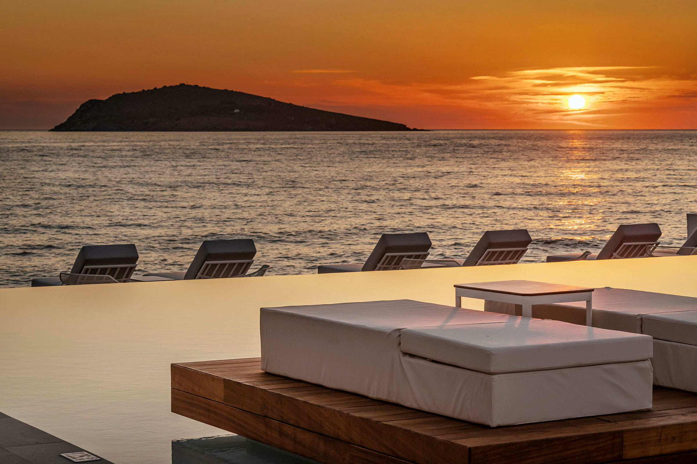 Solnedgång över havet med solstolar vid en infinitypool. (AI-genererad text)