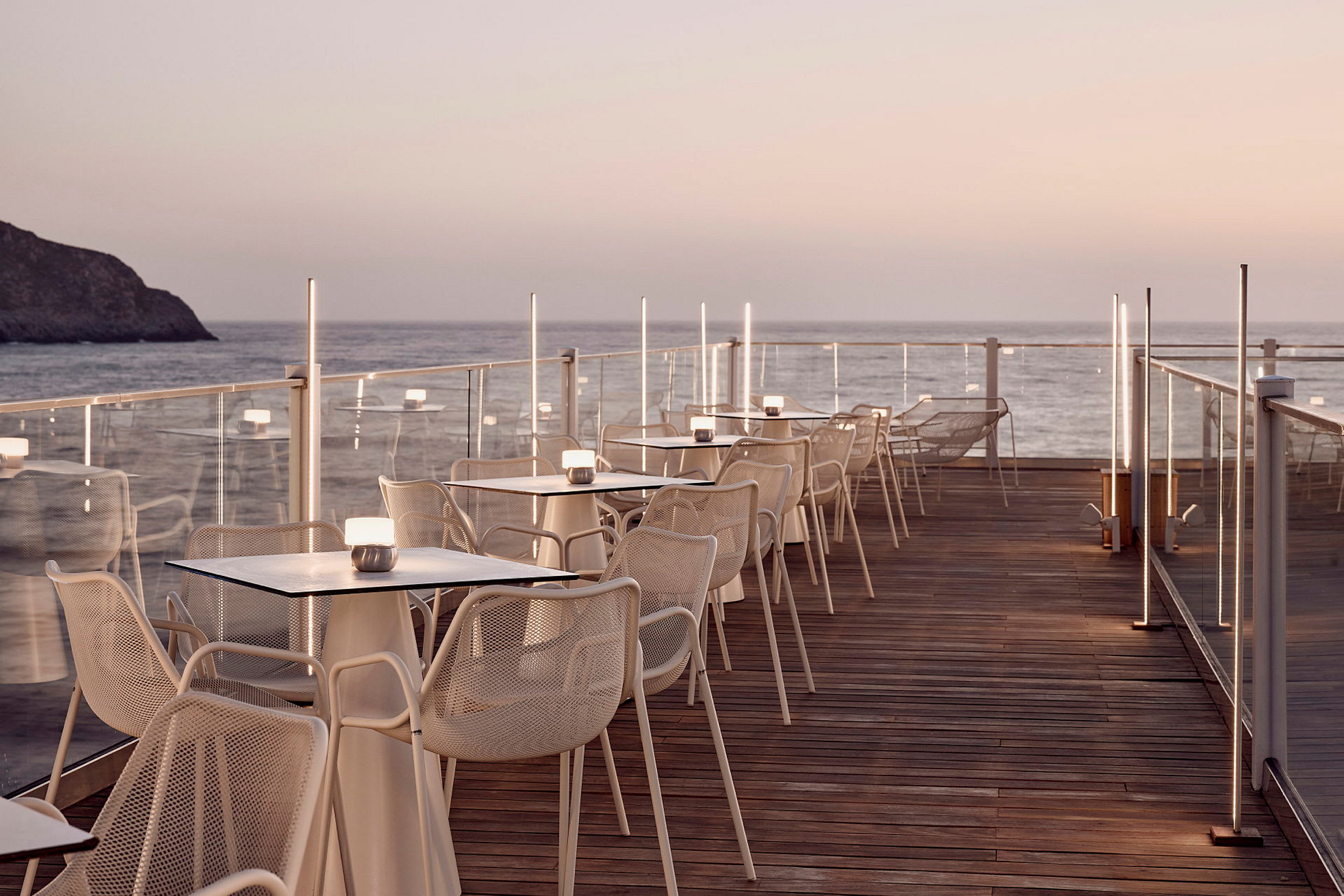 En terrass med bord och stolar vid havet och solnedgång. (AI-genererad text)