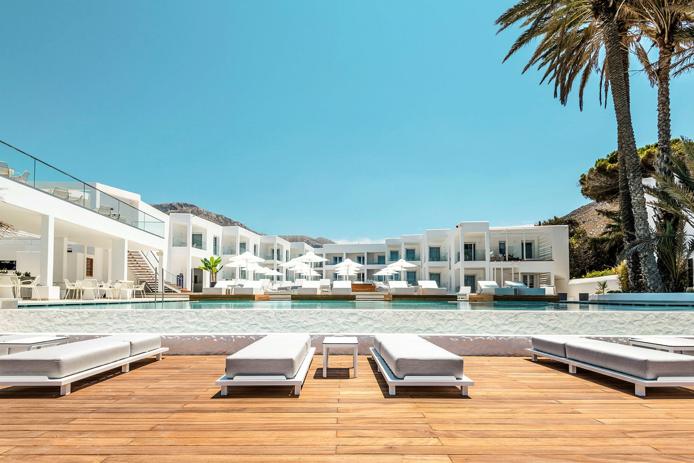 Bild föreställer ett hotellområde med vita byggnader, solstolar och pool. (AI-genererad text)