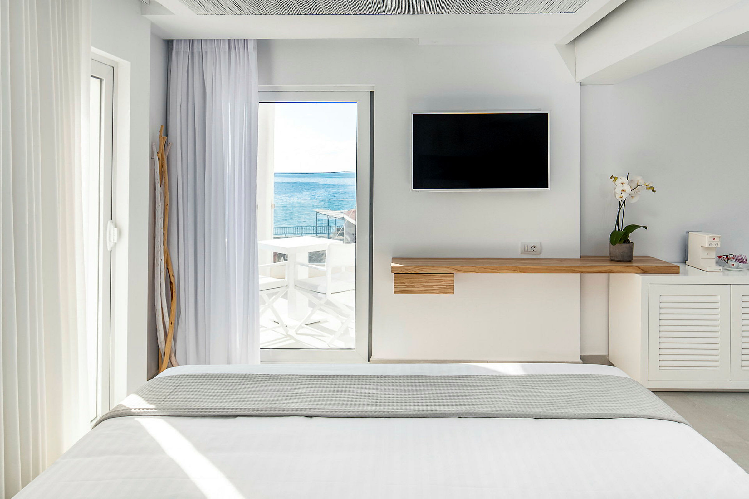 Interiör av ett ljust hotellrum med en säng och havsutsikt genom en glasdörr. (AI-genererad text)