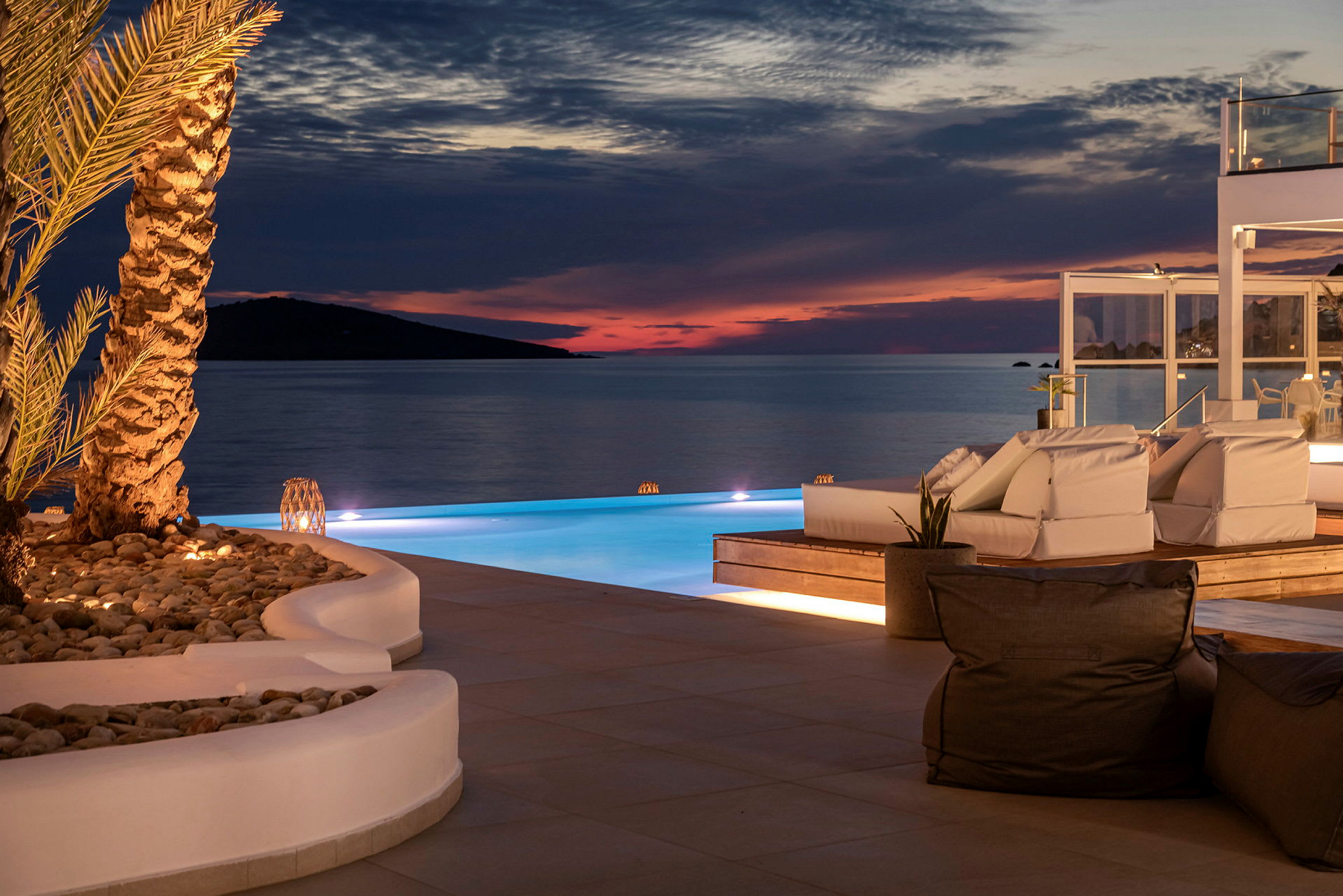 Solnedgång vid infinitypool med loungemöbler och stilfull belysning. (AI-genererad text)