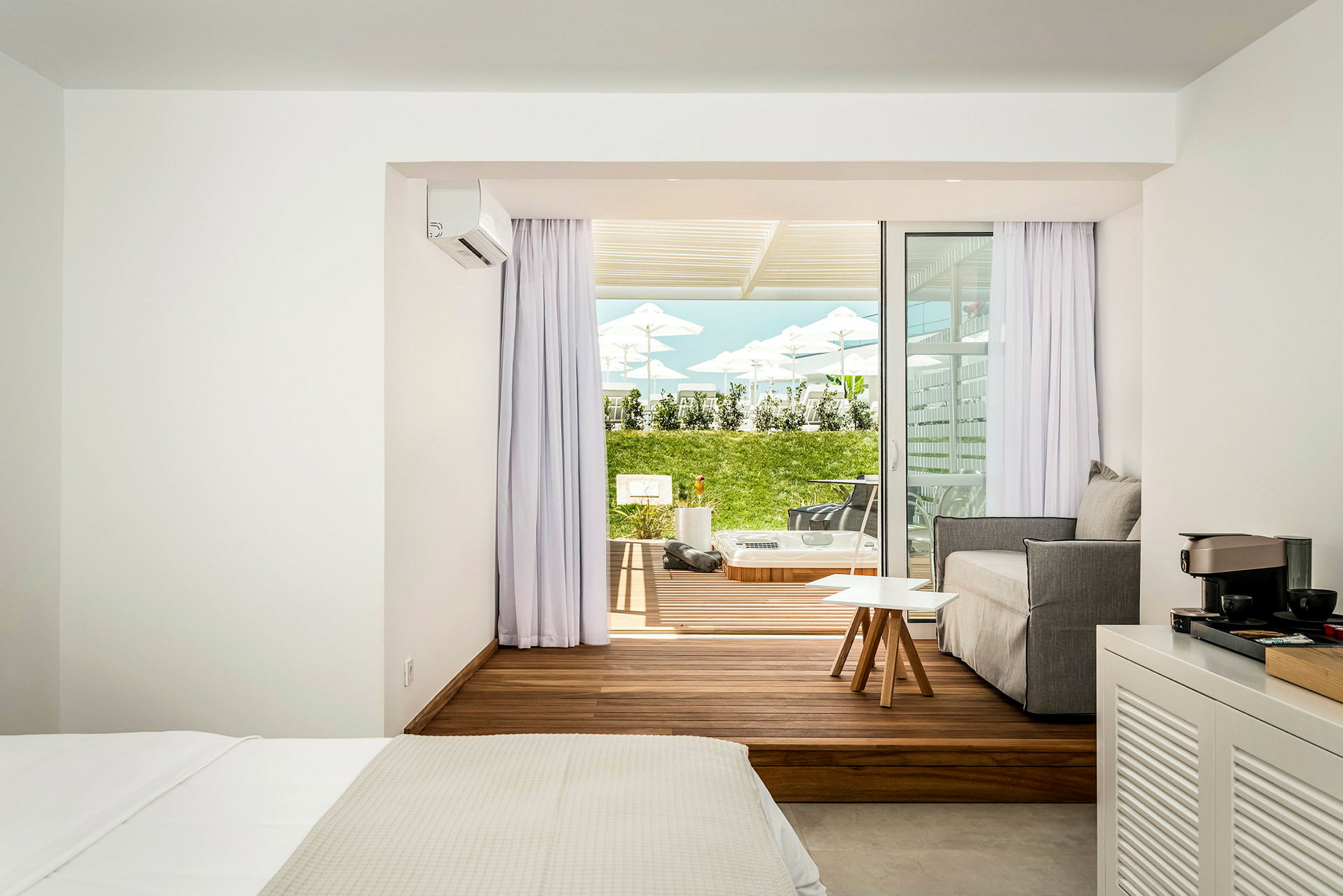 Ett hotellrum med ett modernt sovrum och sittgrupp samt en terrass utanför med gräsmatta och solstolar. (AI-genererad text)
