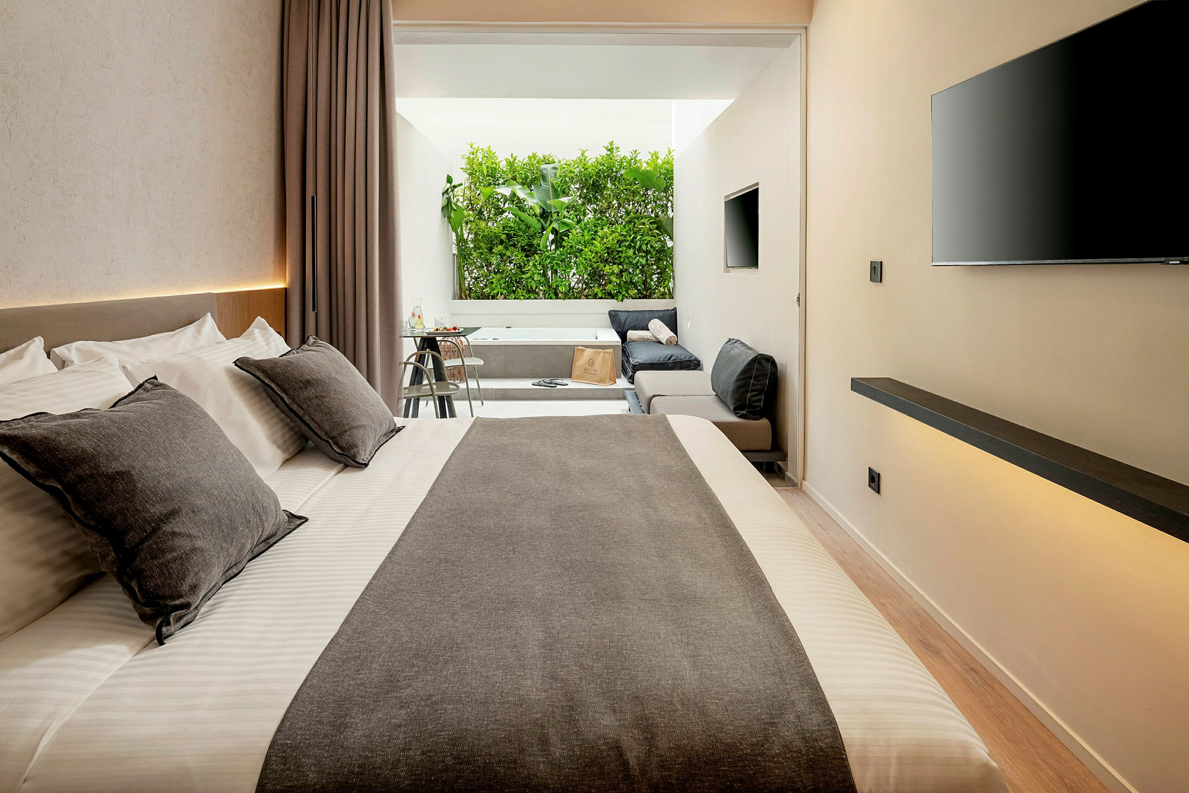 Modern hotelrum med stor säng, sittgrupp och utsikt över grönska. (AI-genererad text)