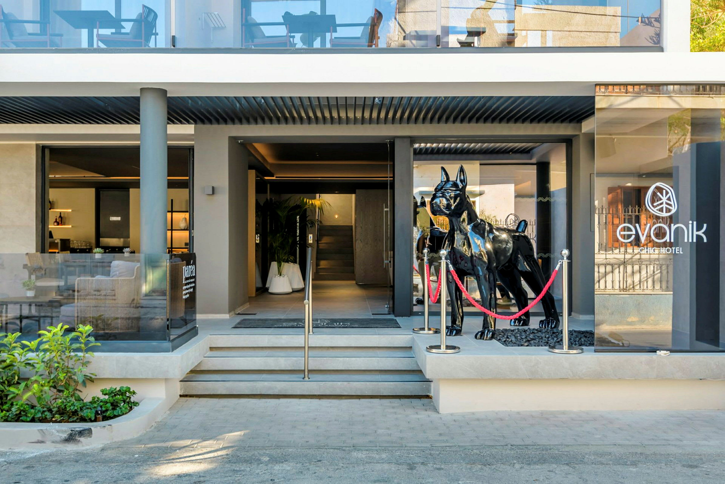 Entrén till Evanik Chic Hotel med en stor svart skulptur av en hund framför glasdörrarna. (AI-genererad text)