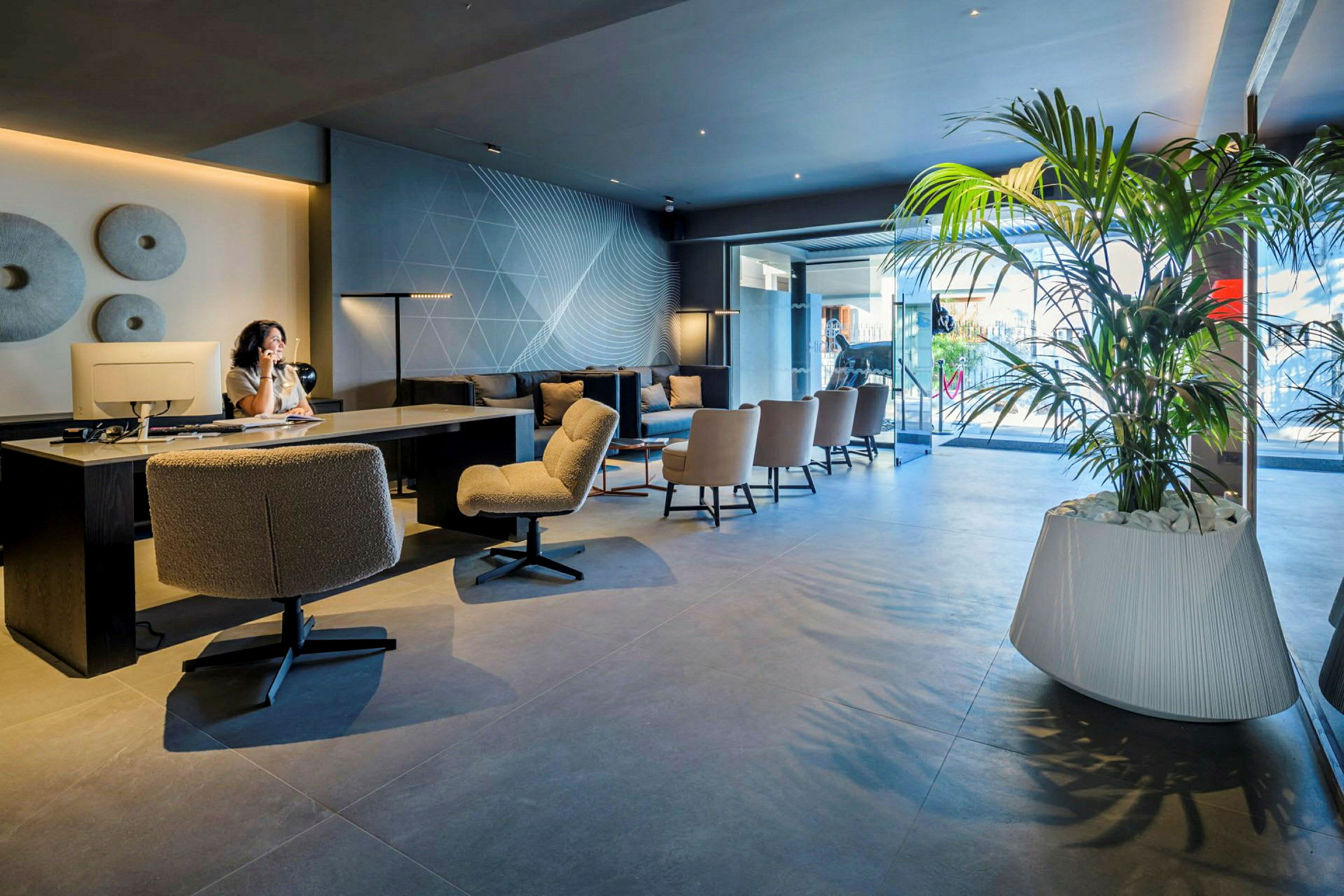 Interiör av en modern lobby med sittplatser, skrivbord och stora gröna växter. (AI-genererad text)