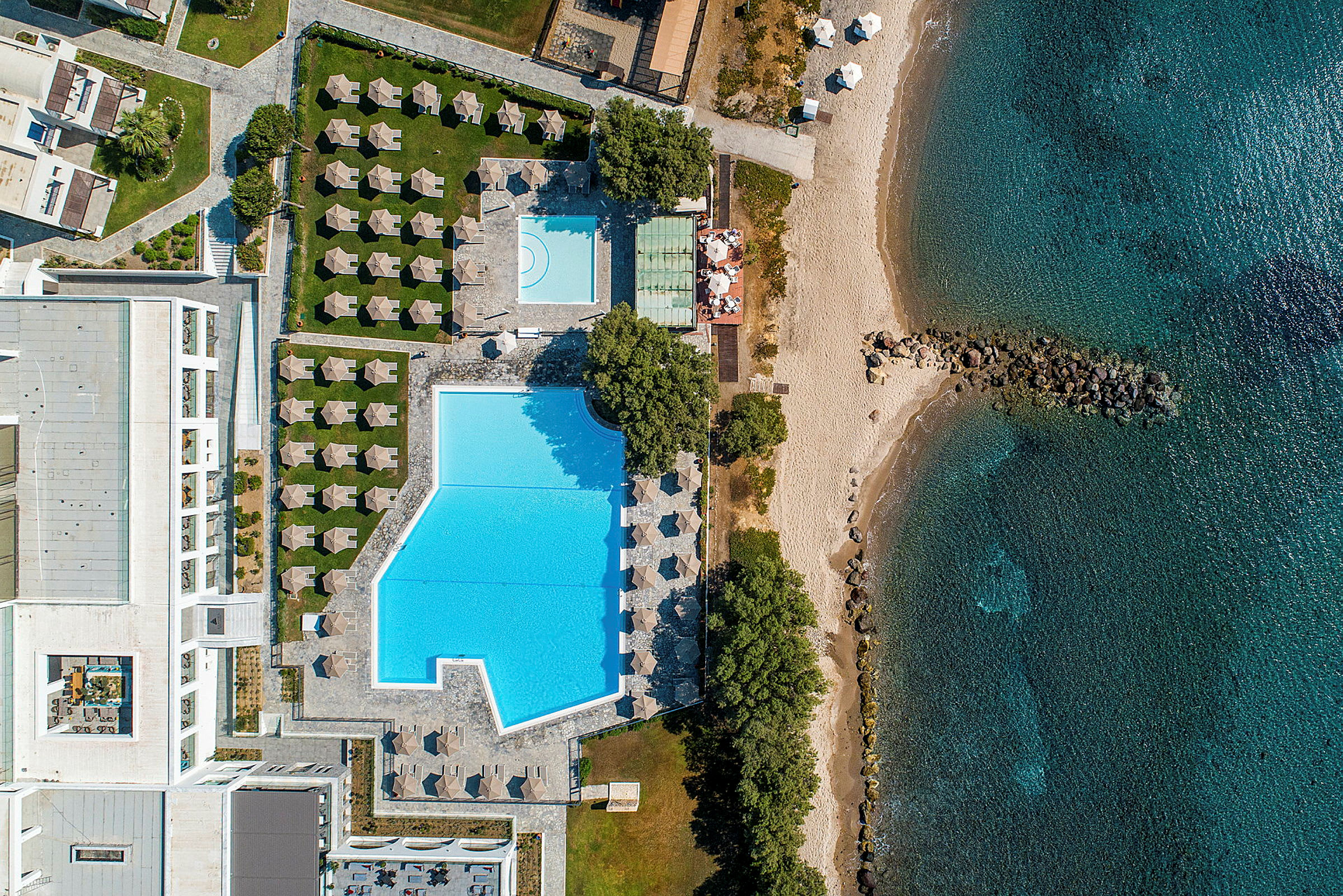 Flygbild över en strand med parasoller, en pool och omgivande grönska. (AI-genererad text)