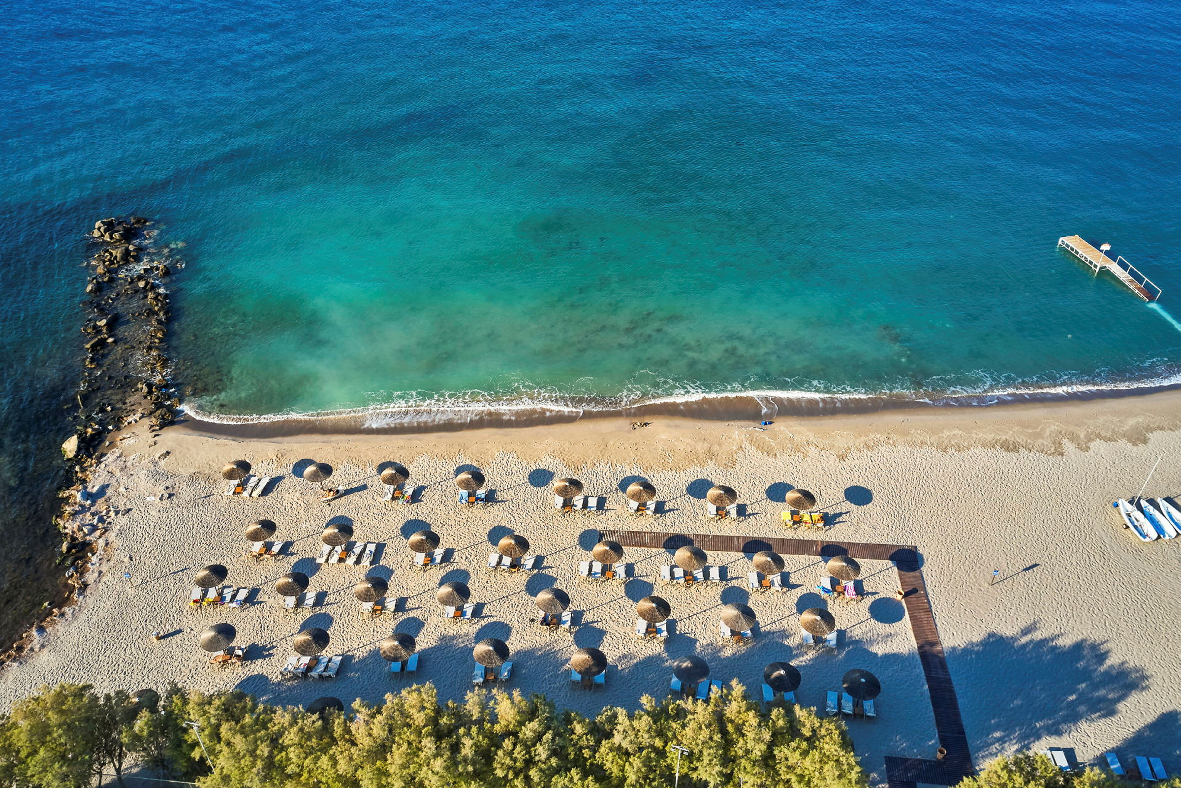 Flygfoto av en sandstrand med parasoller arrangerade i rader nära vattenkanten. (AI-genererad text)